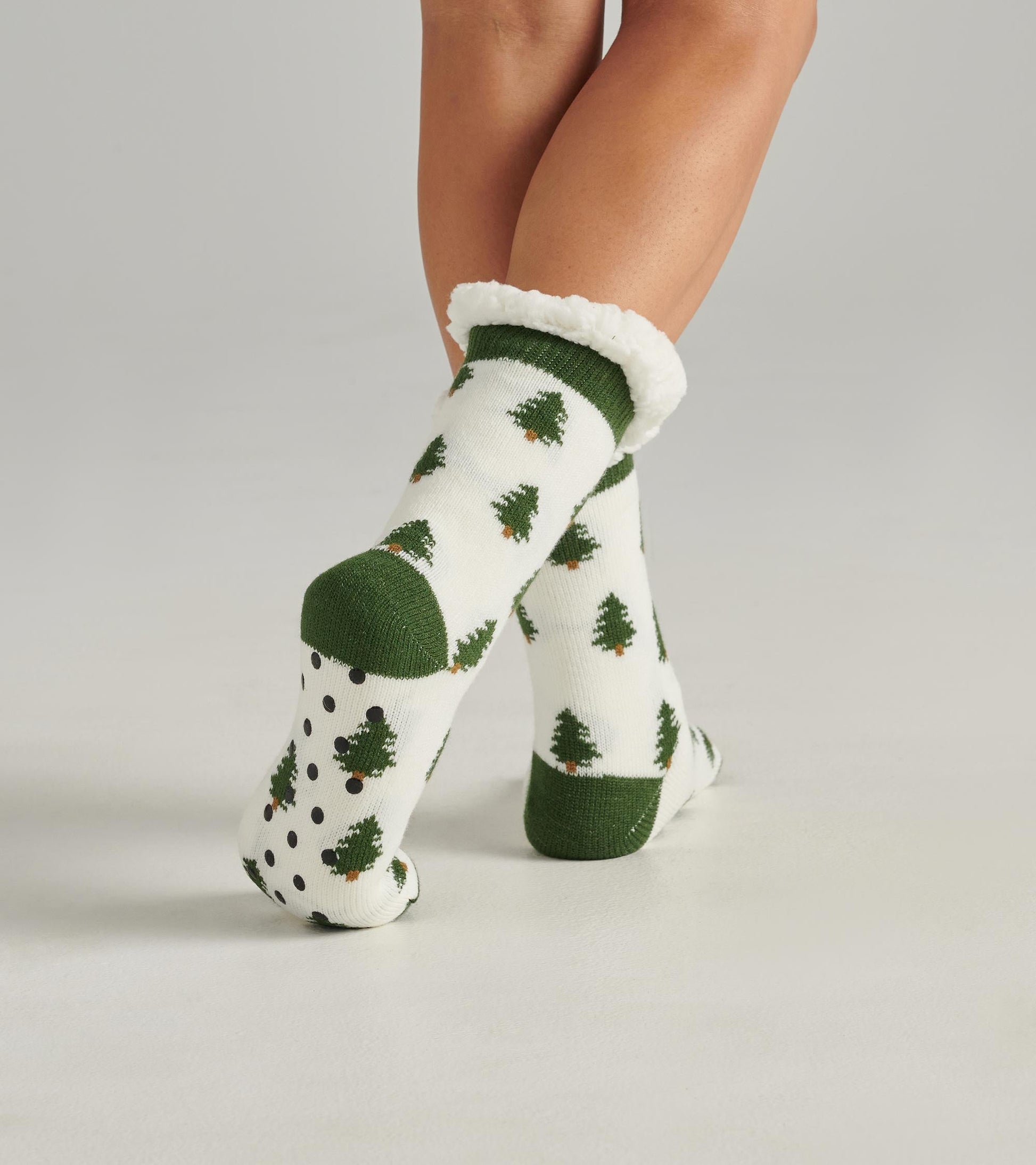 White socks with green tree patterns and green accents, featuring a fluffy cuff and dotted soles.