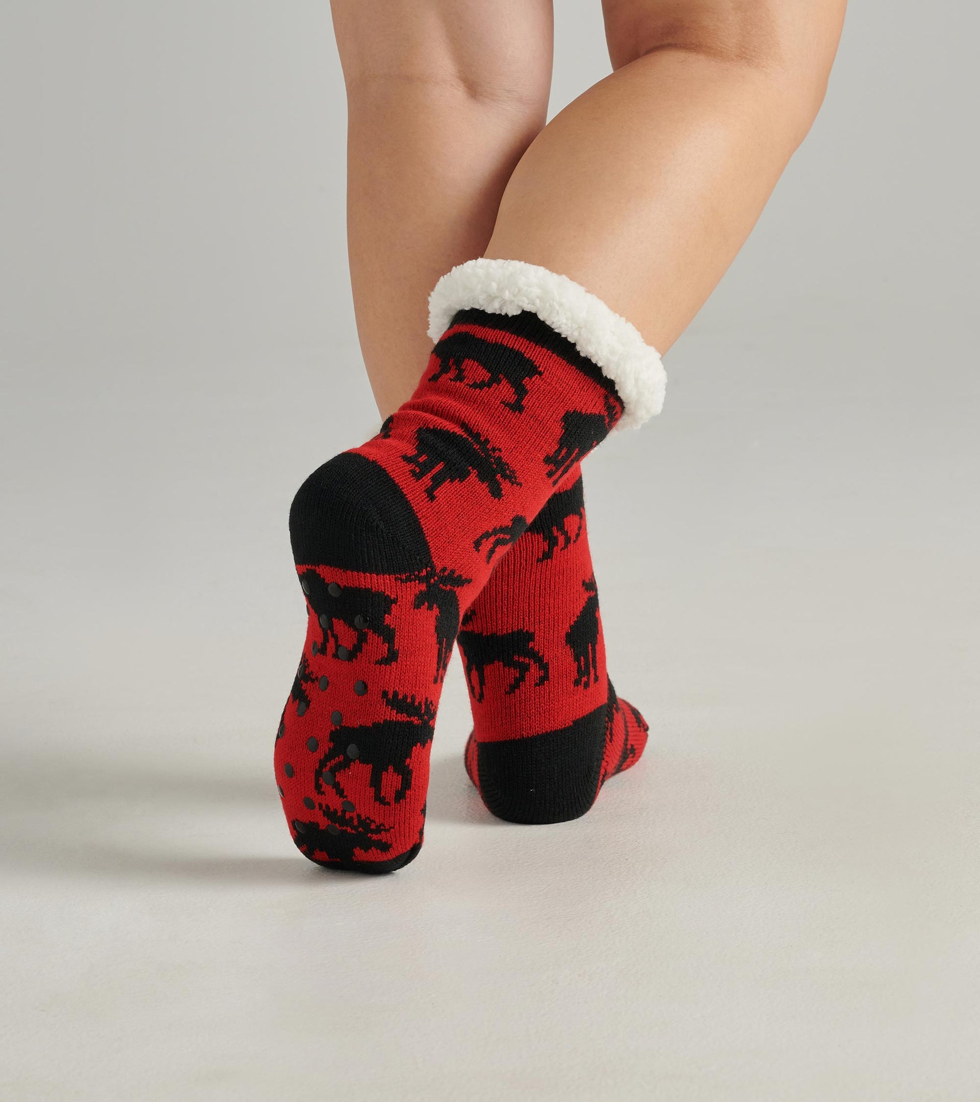 Red cabin socks featuring a moose pattern and a cozy white sherpa lining at the cuff. One size fits most.