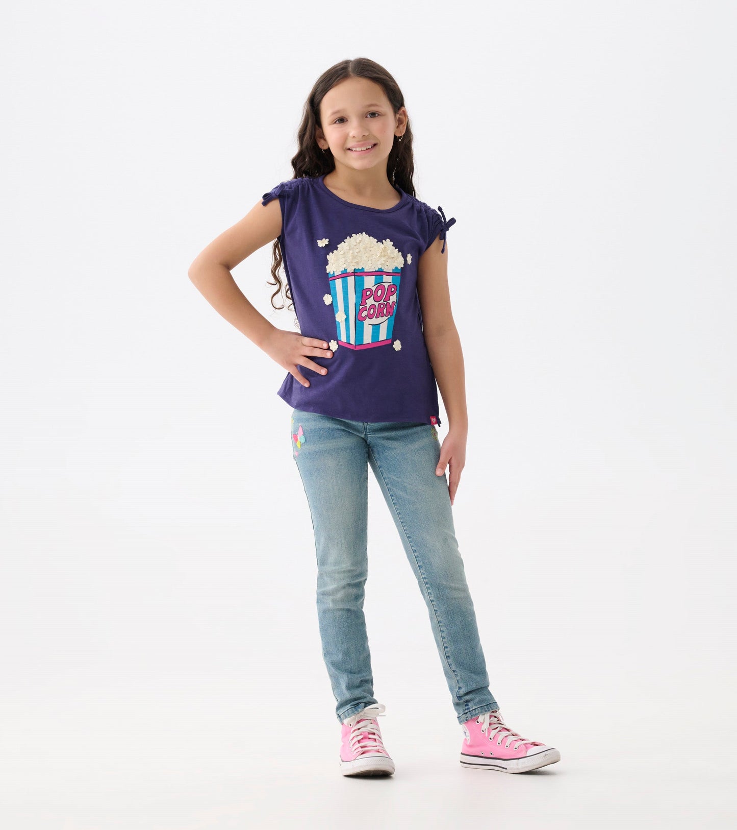 Light blue stretch jeans with colorful patches, fitted style, worn with a purple graphic tee and pink sneakers.