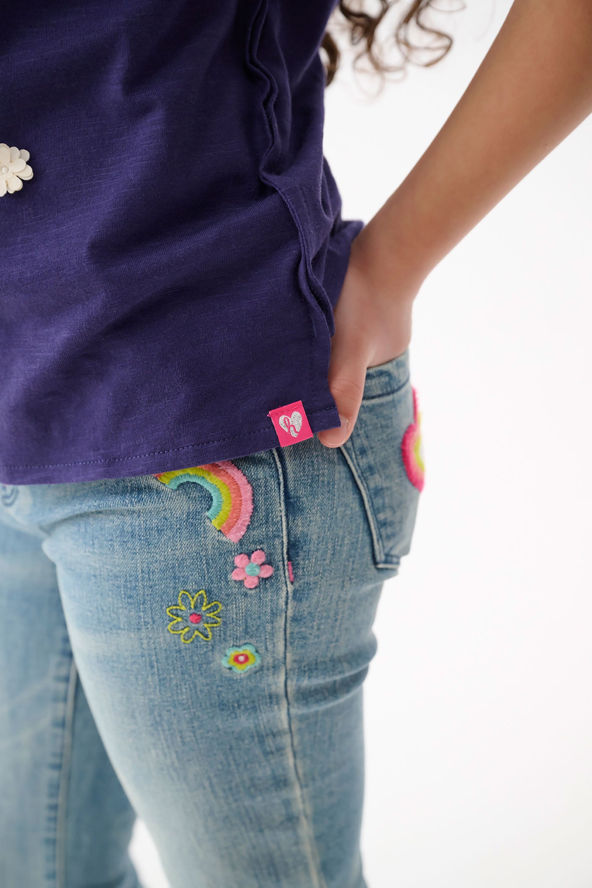 Light blue stretch jeans with colorful embroidered patches of flowers and rainbows, shown from the side.