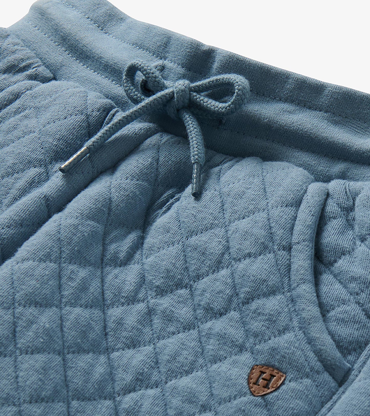 Close-up of faded blue quilted joggers showing the drawstring waistband and small H patch