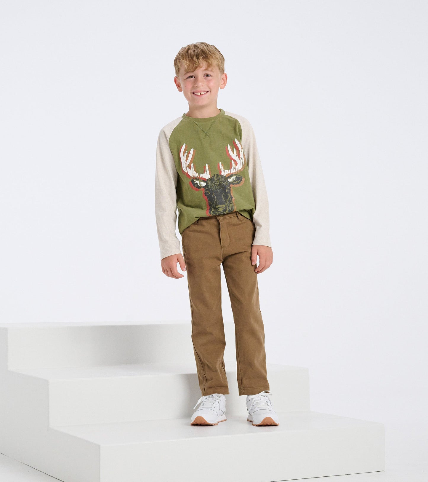 Khaki twill pants on a boy, paired with a green long-sleeve shirt, standing on steps with a neutral background.
