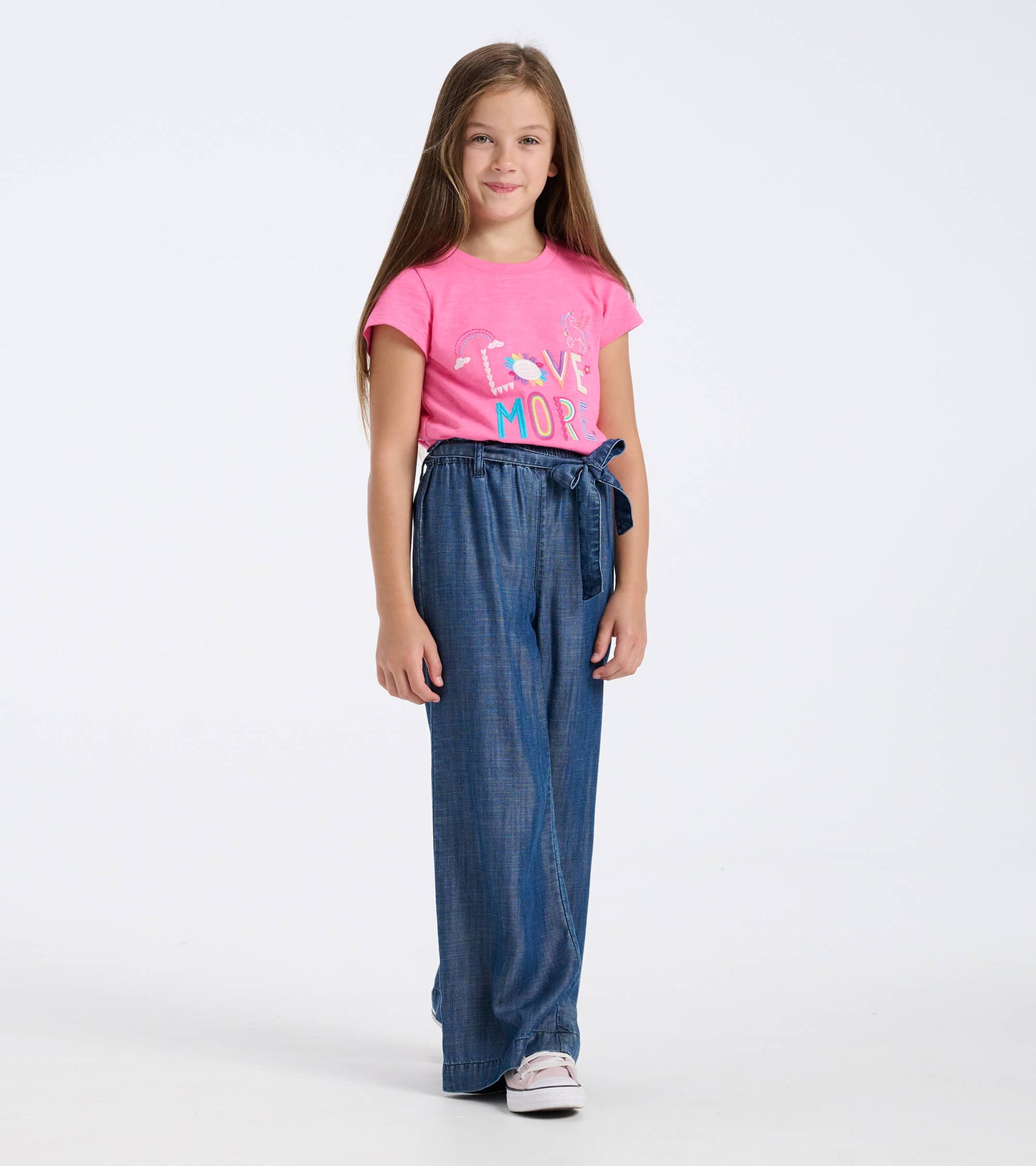Blue textured paperbag pants with a tie waist, paired with a pink graphic t-shirt, worn by a girl standing.