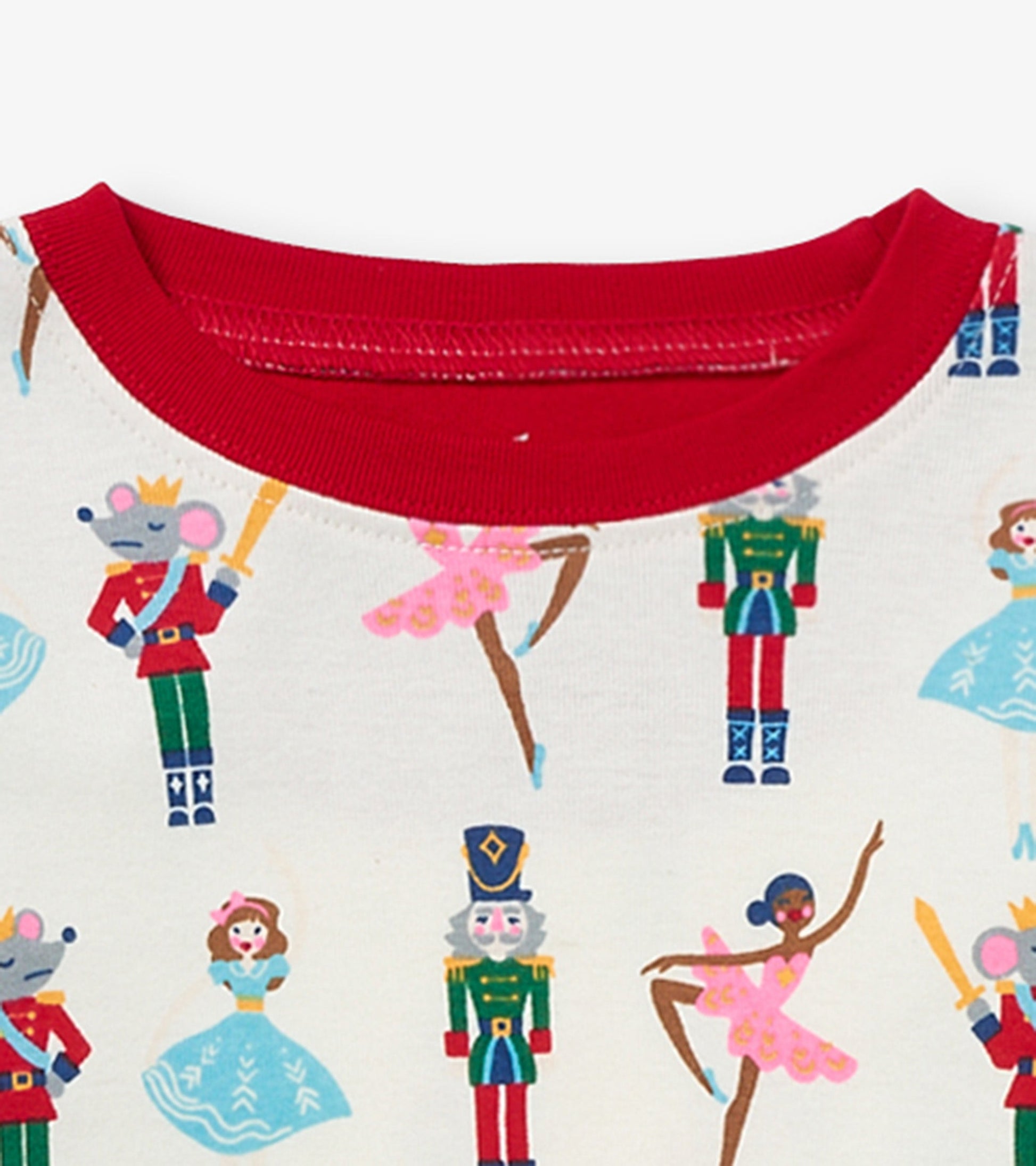 Red-trimmed organic cotton pajama set featuring colorful nutcracker and ballet-themed prints on a cream background.