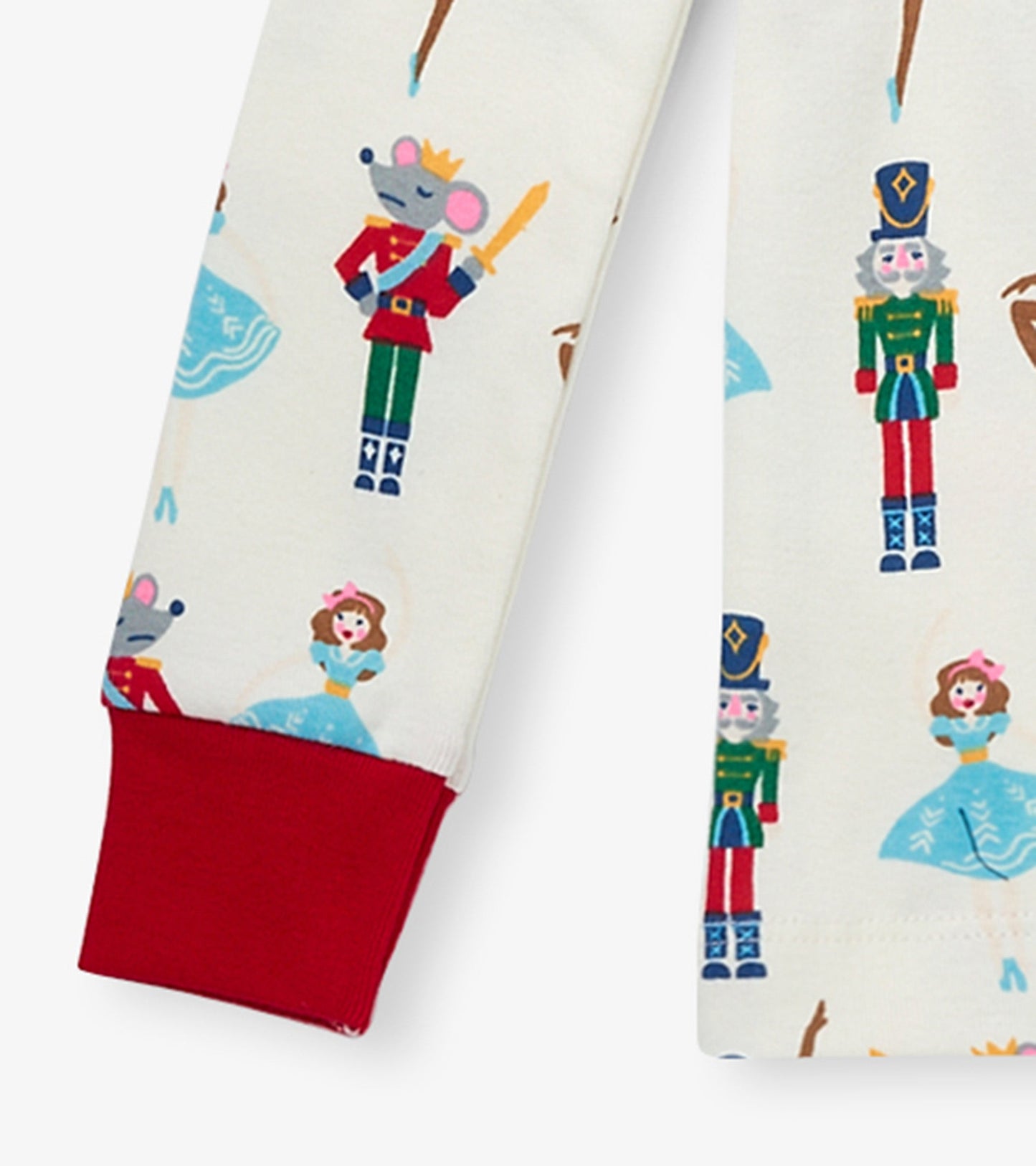 Organic cotton pajama set featuring colorful nutcracker and princess prints on a cream background with red cuffs.