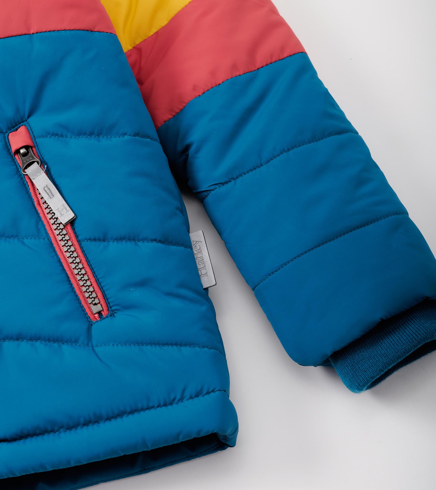 Colour block puffer jacket featuring blue, yellow, and pink sections with a zip pocket and ribbed cuffs.