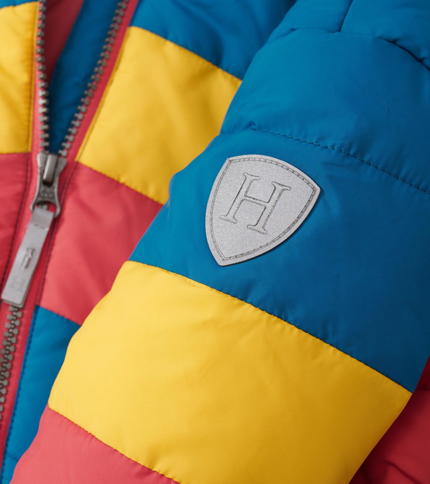 Colour block puffer jacket featuring blue, red, and yellow panels with a logo patch on the sleeve.