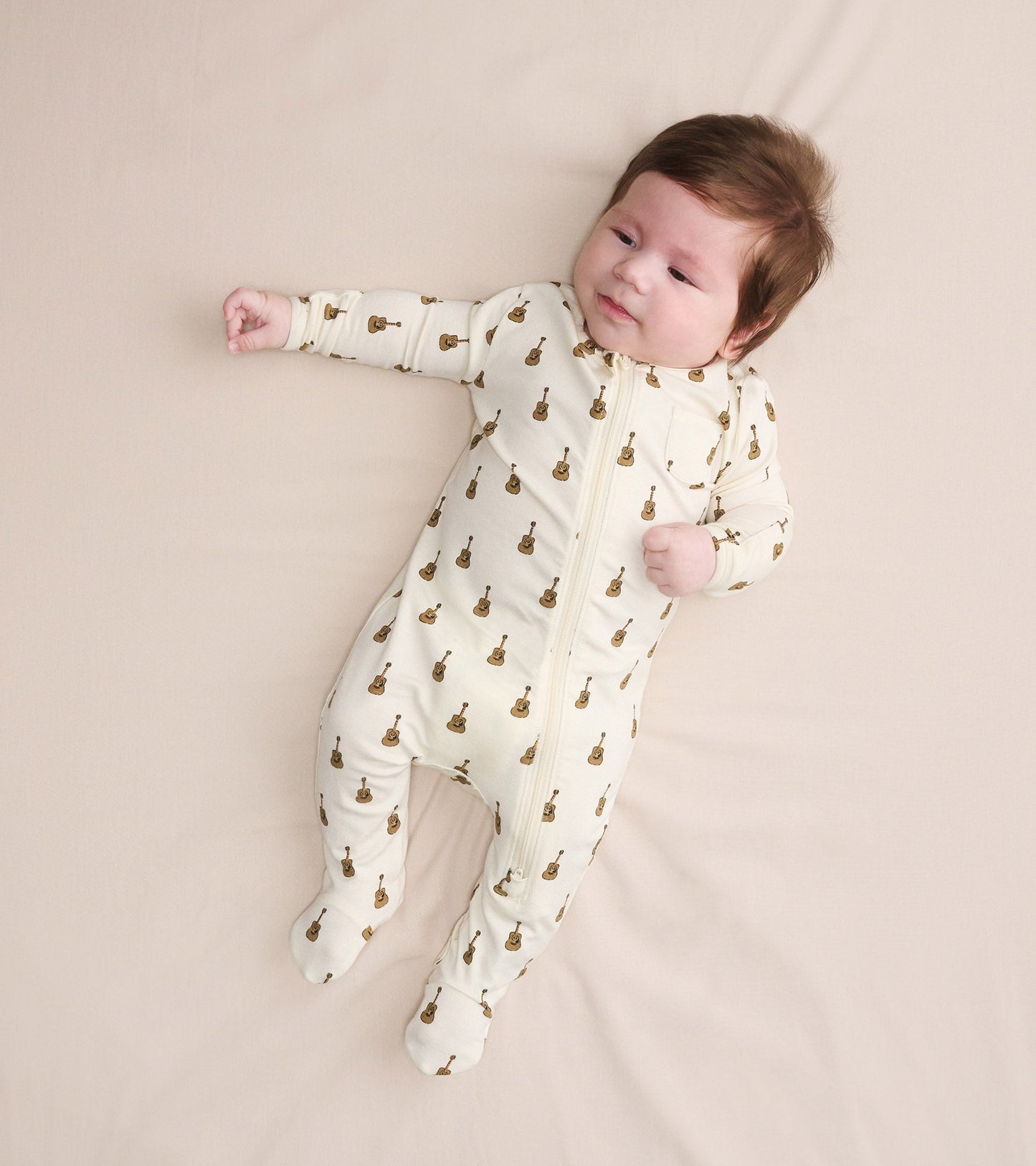 Cream bamboo sleeper for baby boys, featuring a guitar print, with a front zipper and footed design.