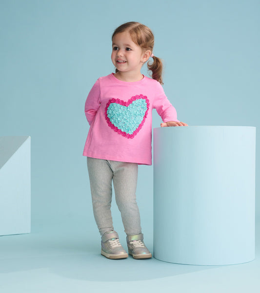 Pink long sleeve t-shirt featuring a textured heart design, paired with gray leggings and silver sneakers.