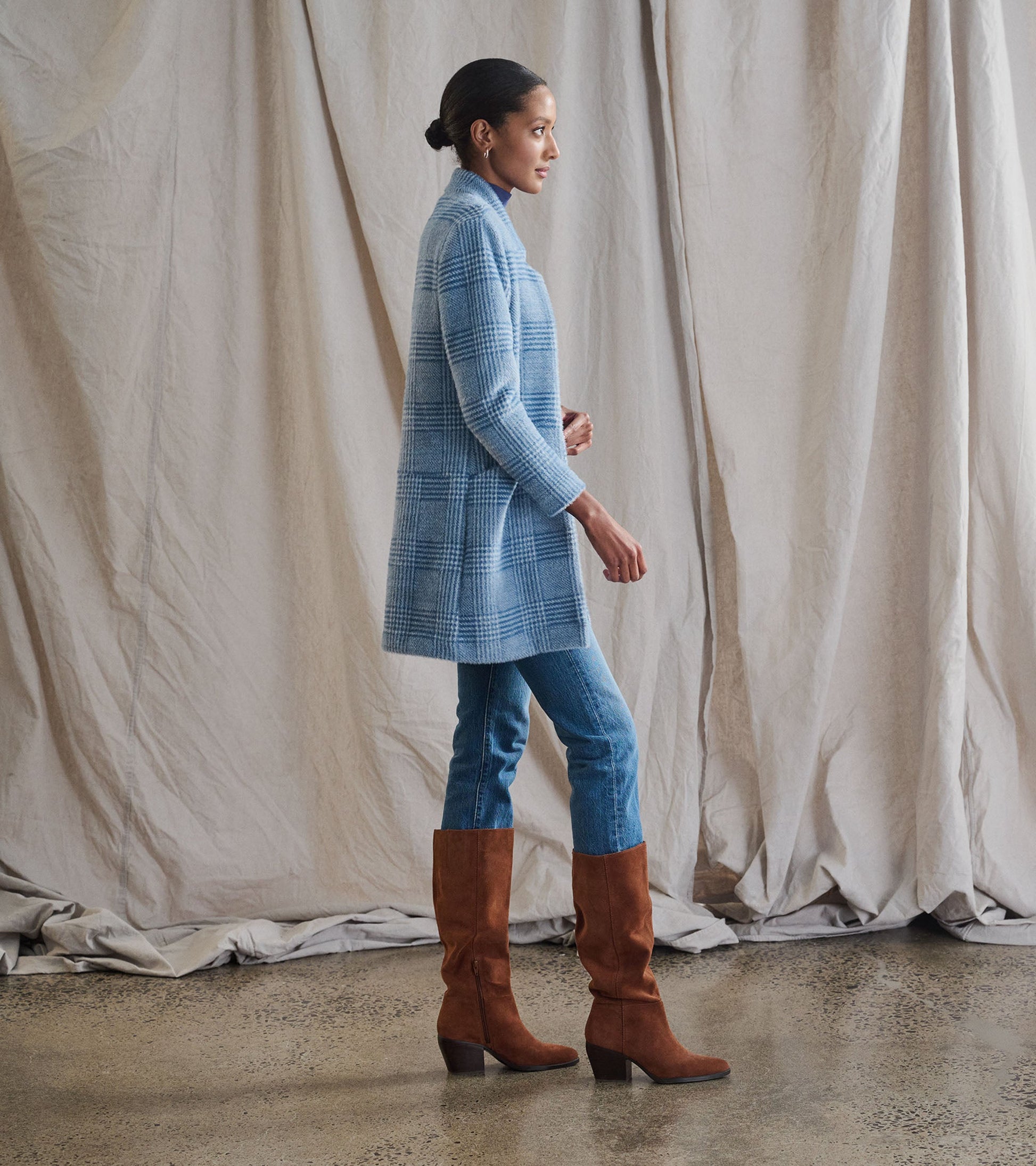 Open front jacket in blue check pattern, styled with fitted jeans and brown knee-high boots, shown from the side.