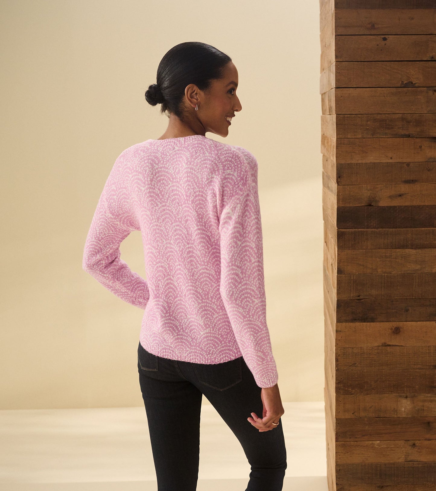 Pink sweater with a deco dot pattern, featuring long sleeves and a relaxed fit, styled with dark jeans.