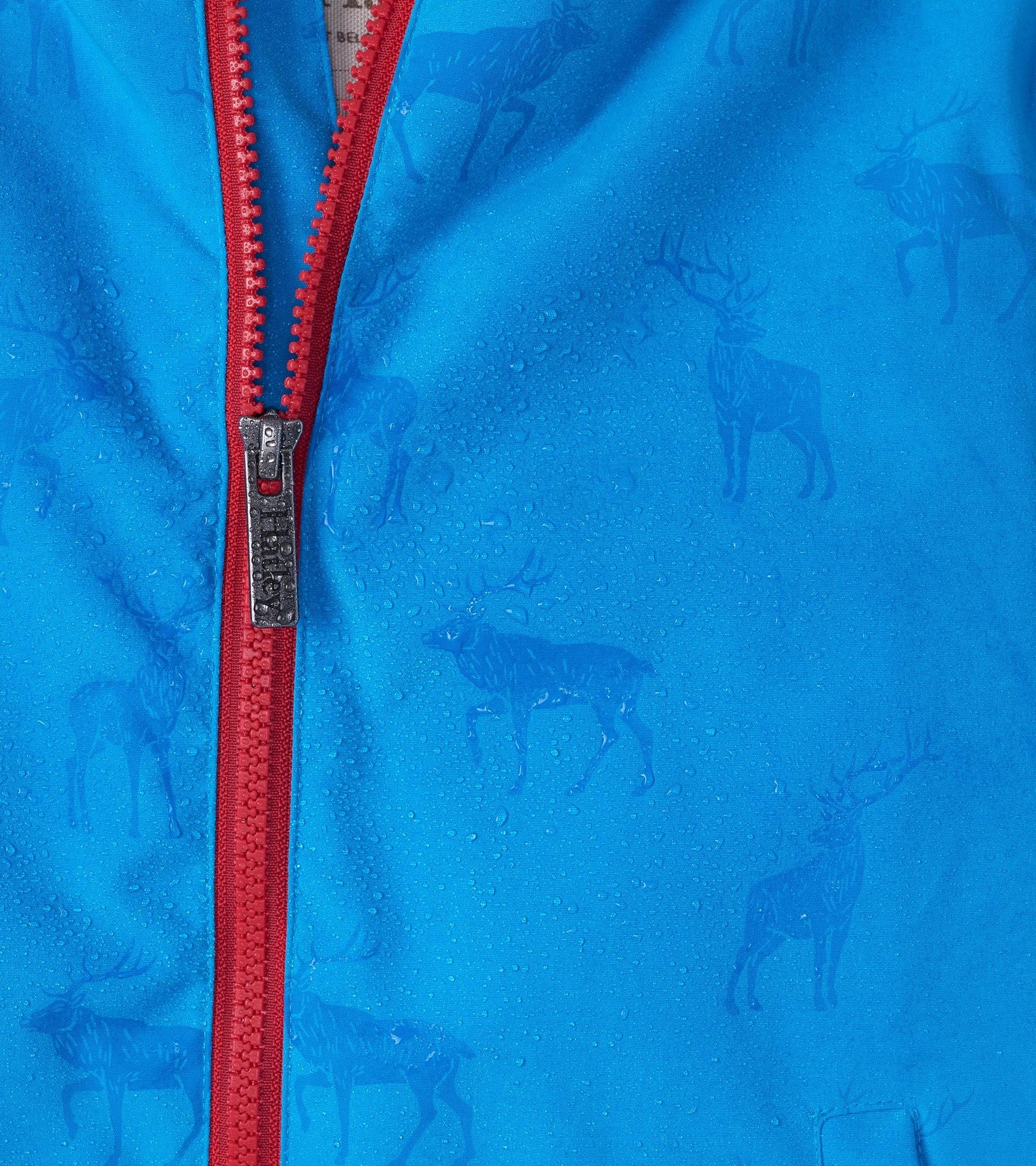 Lightweight blue rain jacket with a red zipper, featuring a subtle elk pattern and water droplets on the surface.
