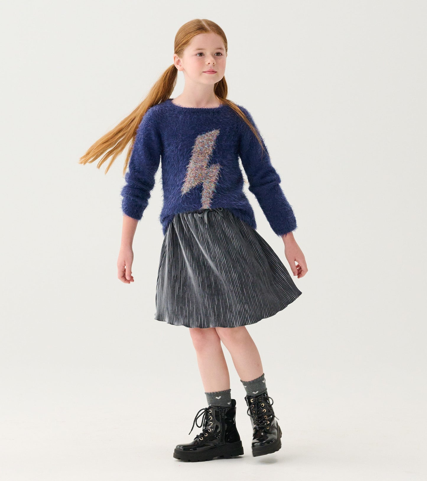 Navy furry sweater with metallic lightning bolt design, paired with a pleated skirt and black lace-up boots.