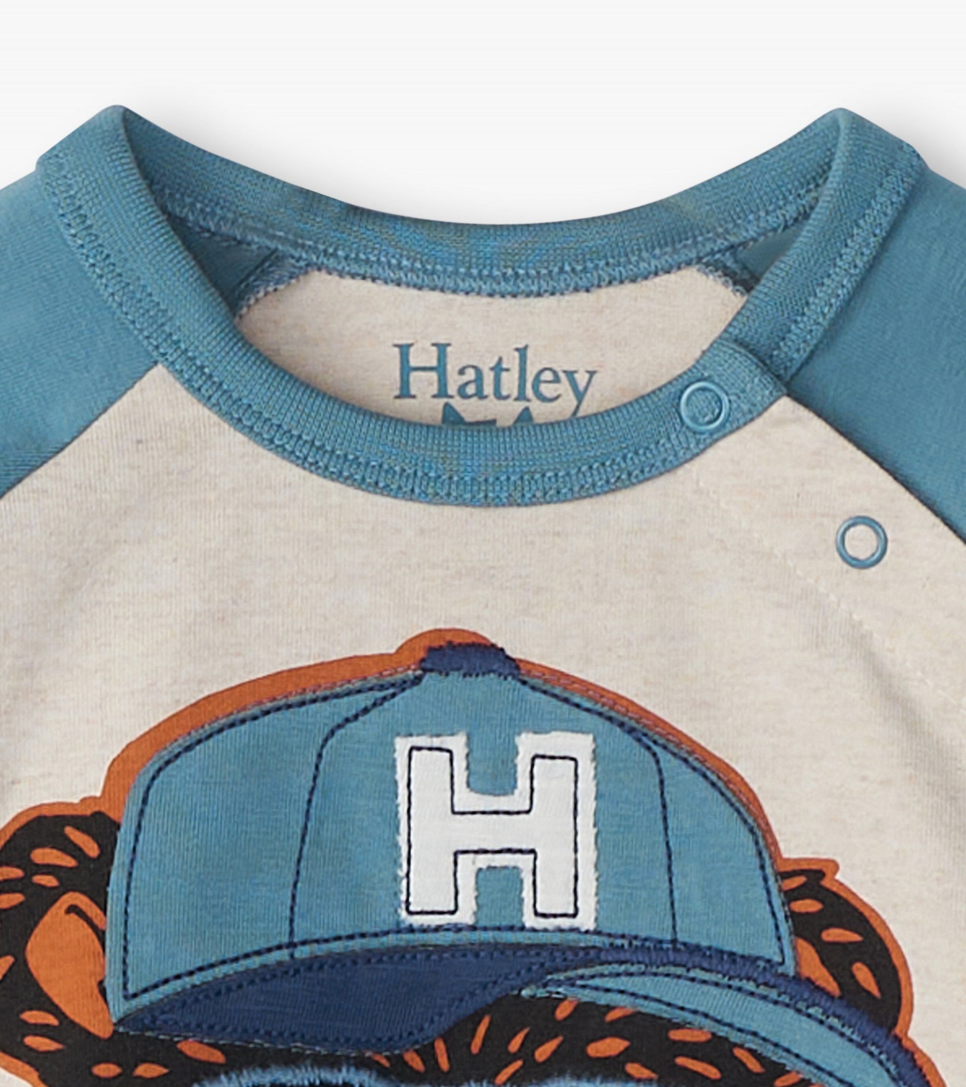 Light beige long sleeve t-shirt with blue raglan sleeves and a bear graphic wearing a cap.