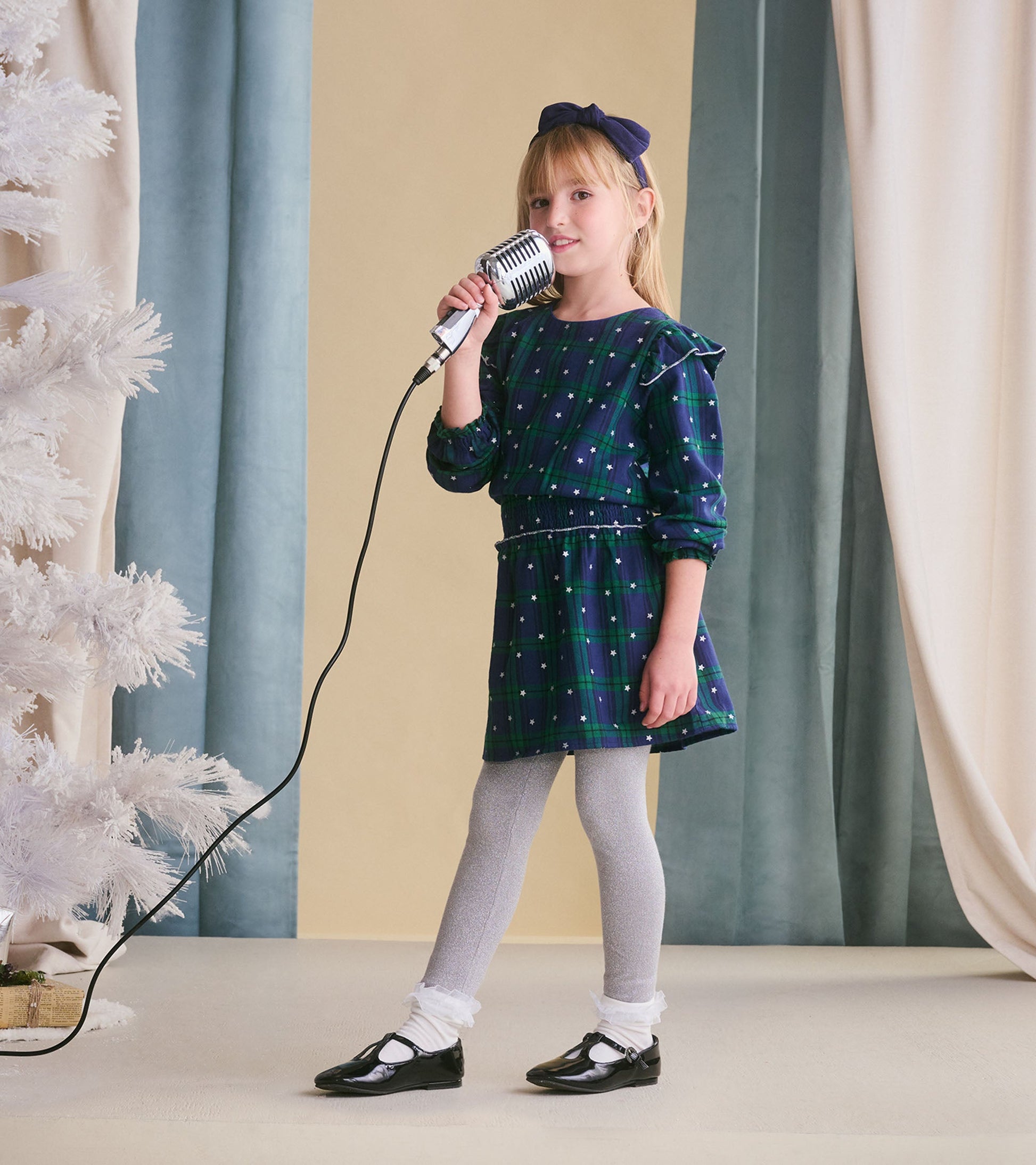 Girls' blackwatch plaid dress with smocked waist, long sleeves, and ruffled details, paired with gray leggings and black sho…