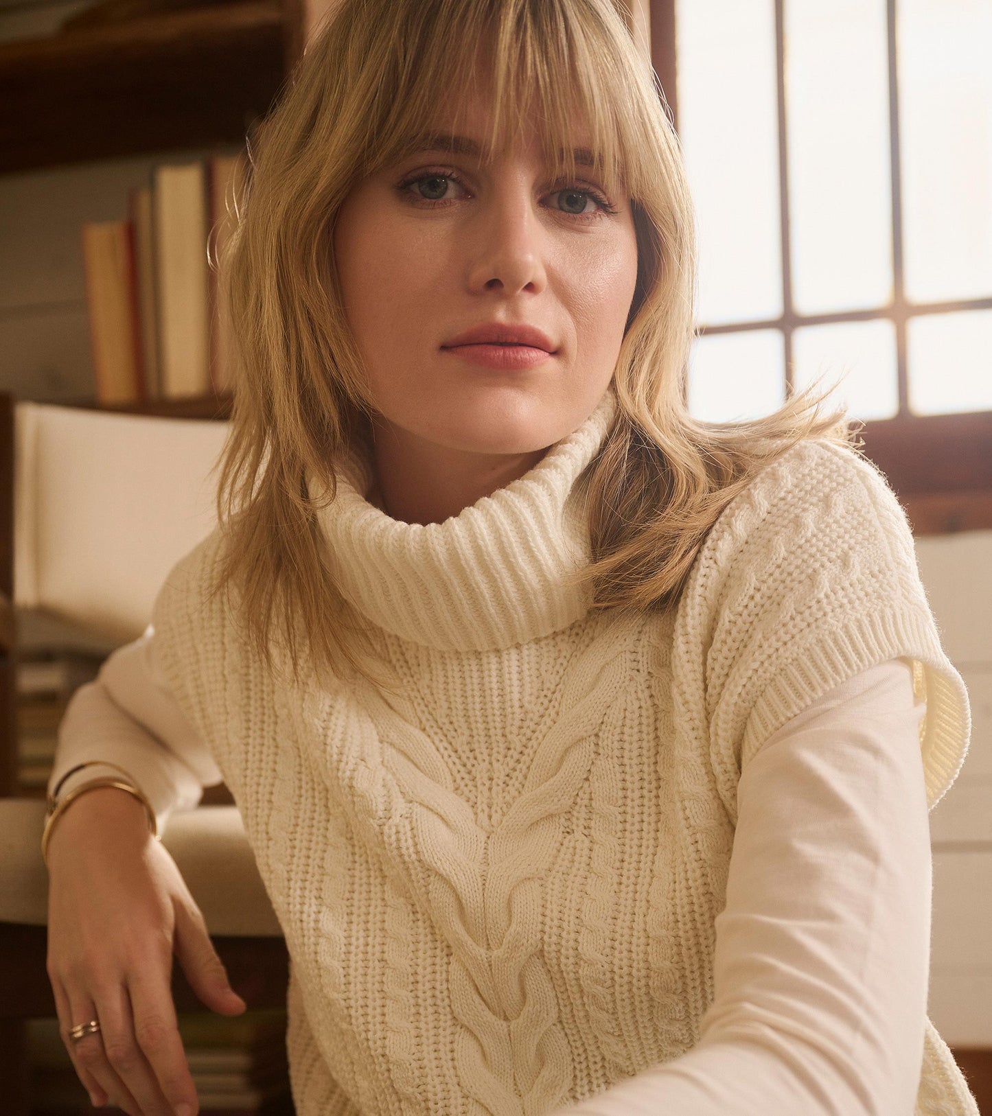 Cable knit vest in winter white with a high collar, featuring a textured pattern, styled over a long-sleeve top.