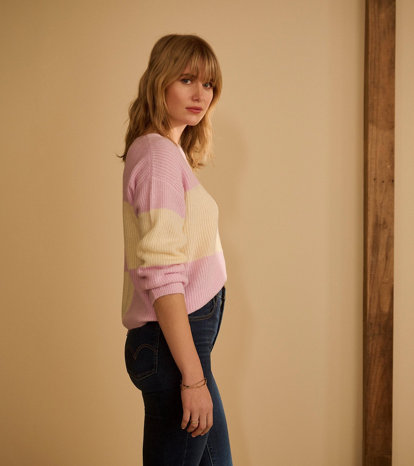 Pink and cream striped sweater with ribbed texture, featuring long sleeves and a relaxed fit, worn with dark jeans.