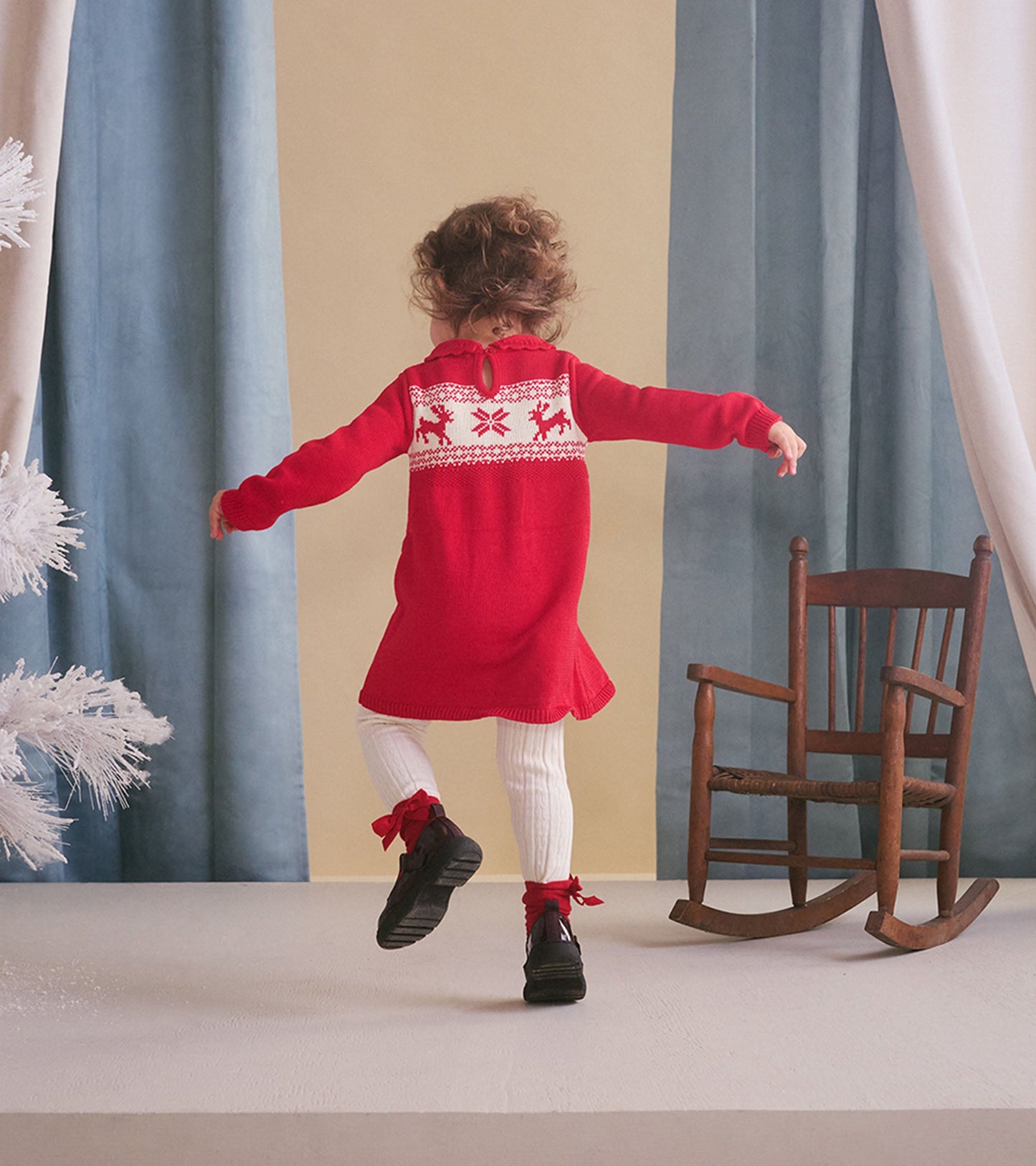 Red cable knit sweater dress with festive pattern, long sleeves, and a back keyhole detail, worn with white tights and black…