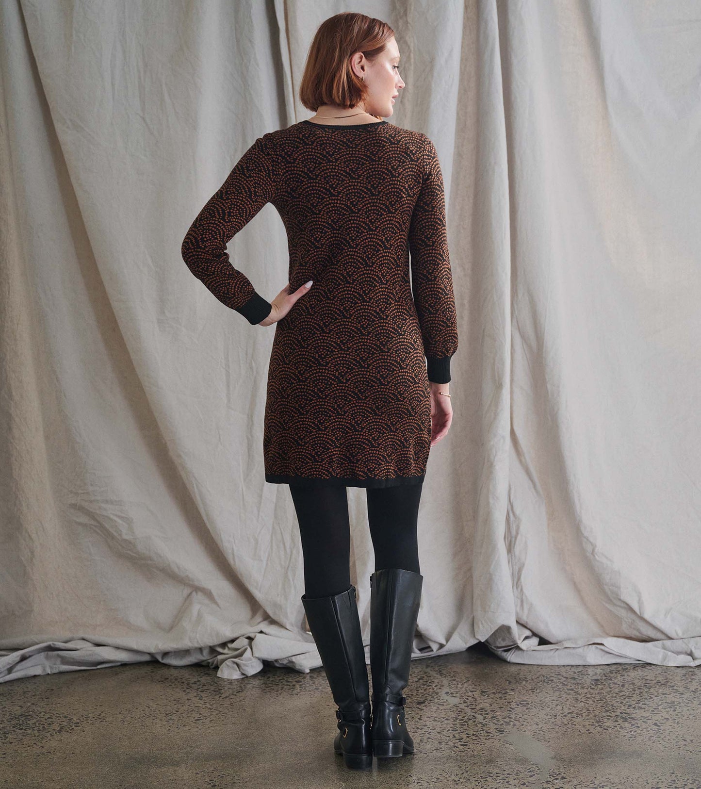 Brown sweater dress with Art Deco dot pattern, long sleeves, and black cuffs, styled with black knee-high boots.