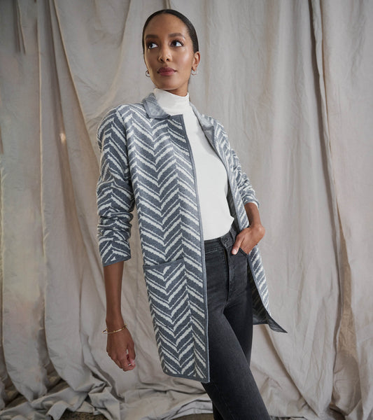 Grey chevron sweater blazer with long sleeves and pockets, styled over a white top and black jeans.