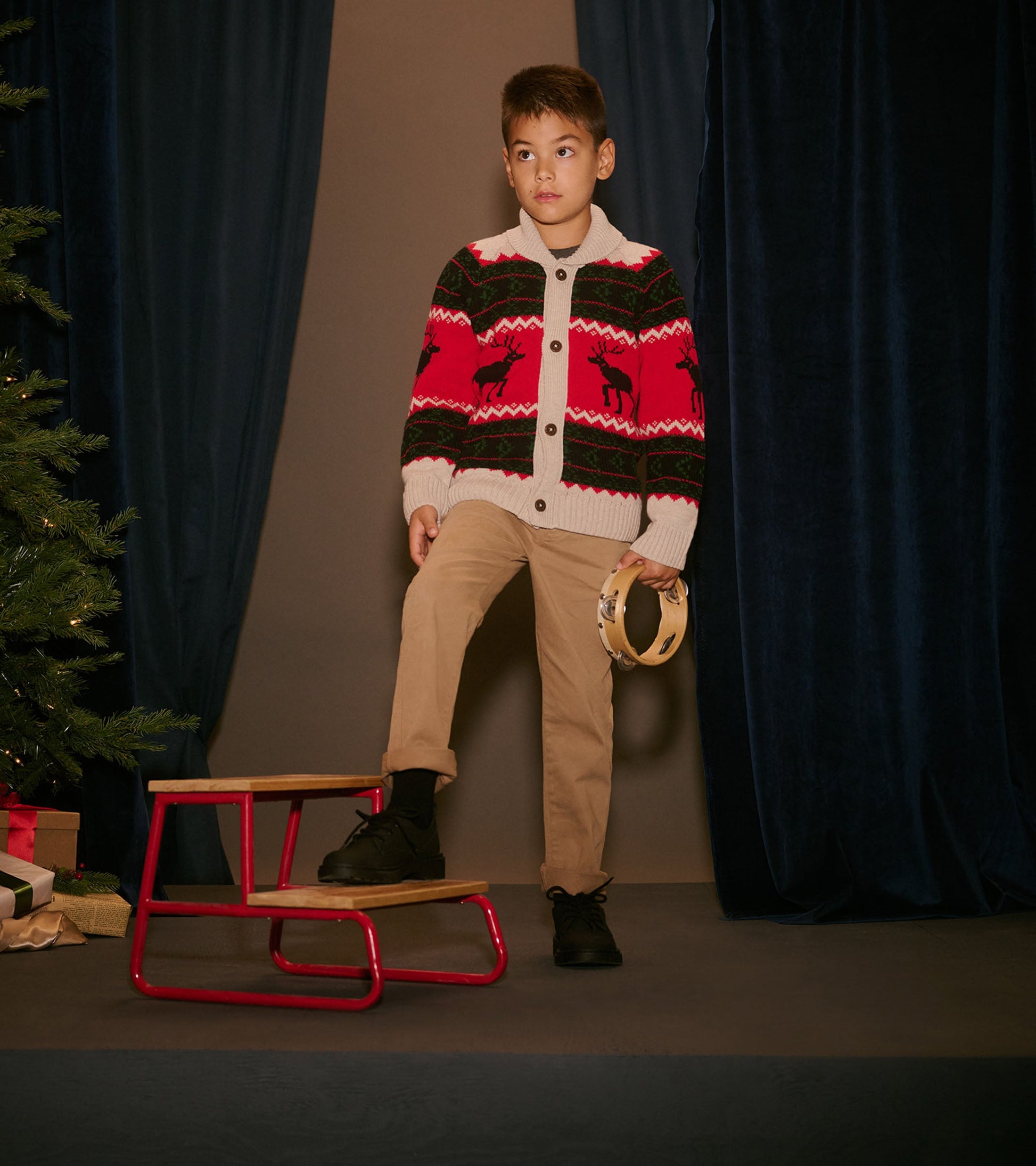 Red and cream shawl collar cardigan with reindeer pattern, worn by a boy standing on a small stool.