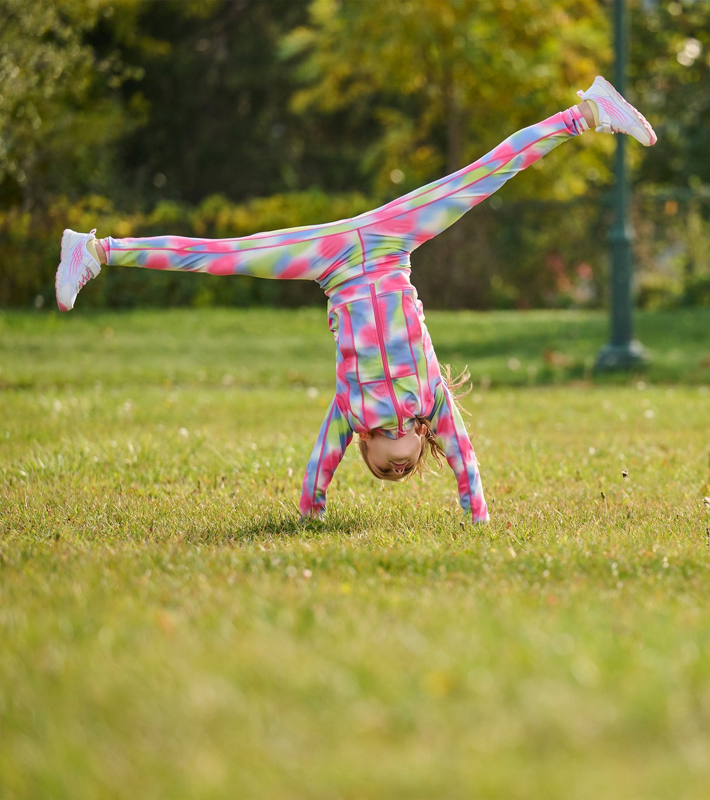 Colorful, tie-dye active jacket with a zip front, worn by a girl doing a handstand on grass.