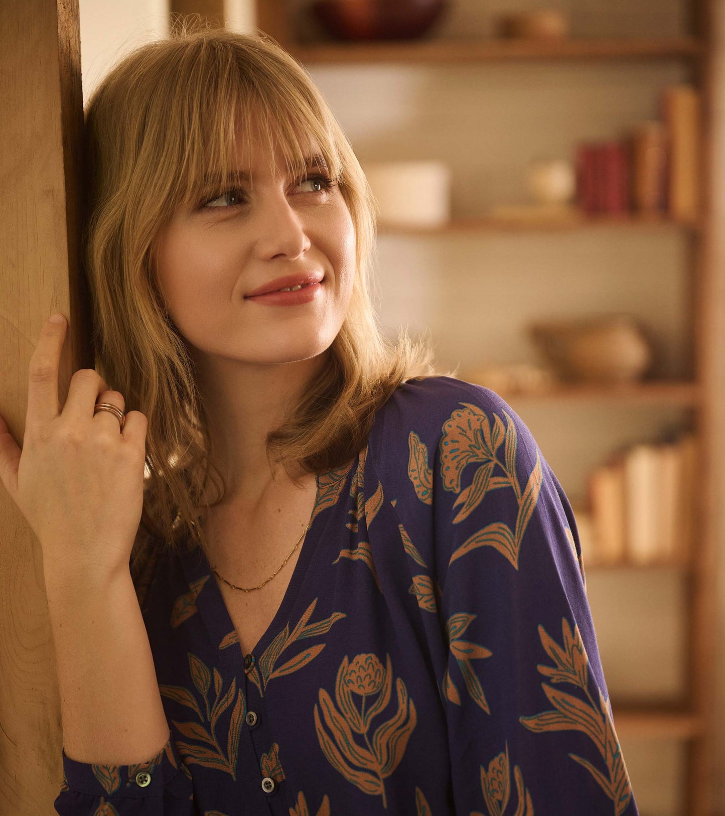 Purple dress with floral pattern, featuring a smocked waist and button details, styled with layered necklaces.