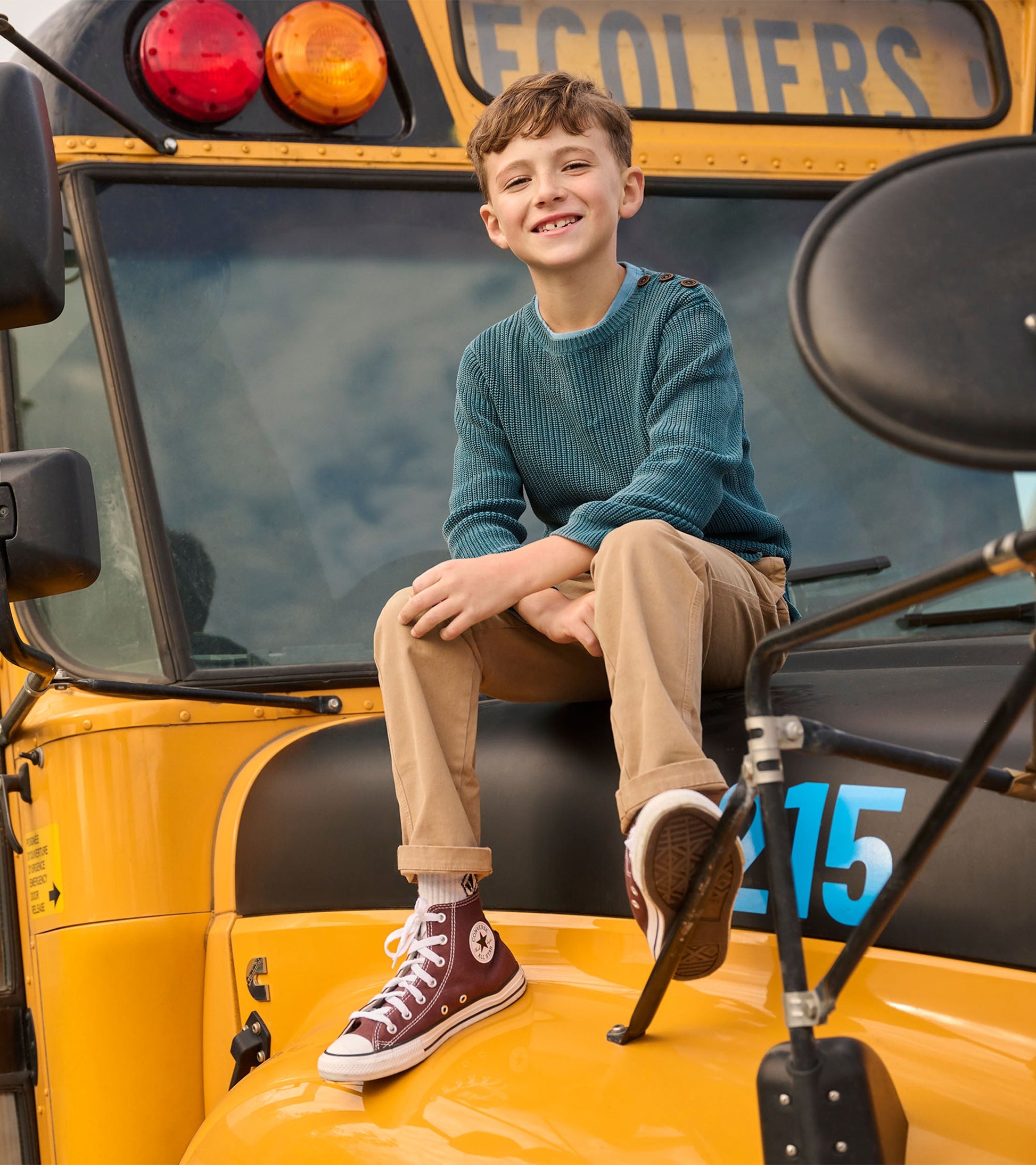 Boys' Moroccan blue sweater with button neck detail, worn by a child sitting on a yellow school bus.
