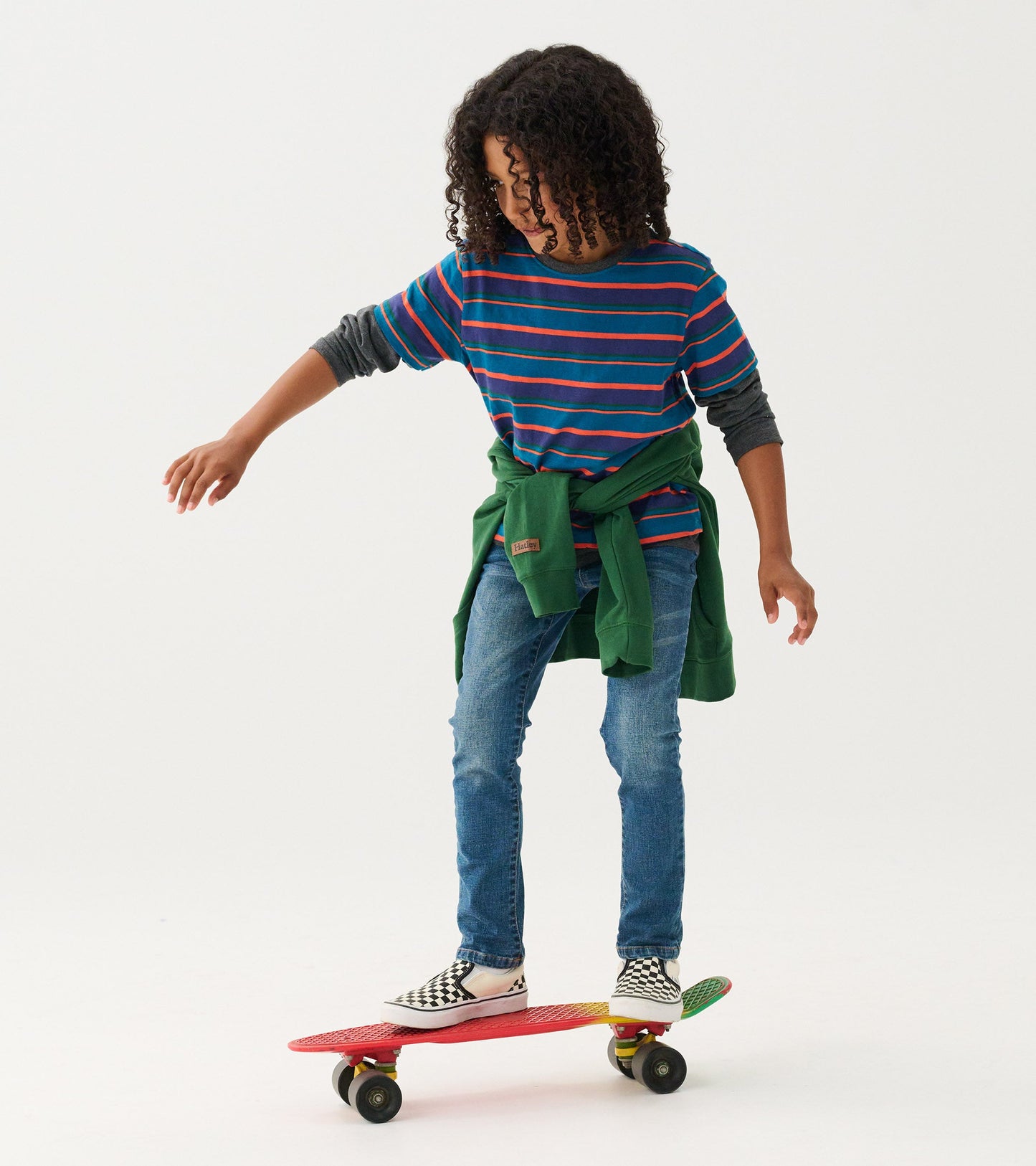 Boys' long sleeve t-shirt in Moroccan blue with colorful stripes, worn with jeans and a green sweater tied around the waist.