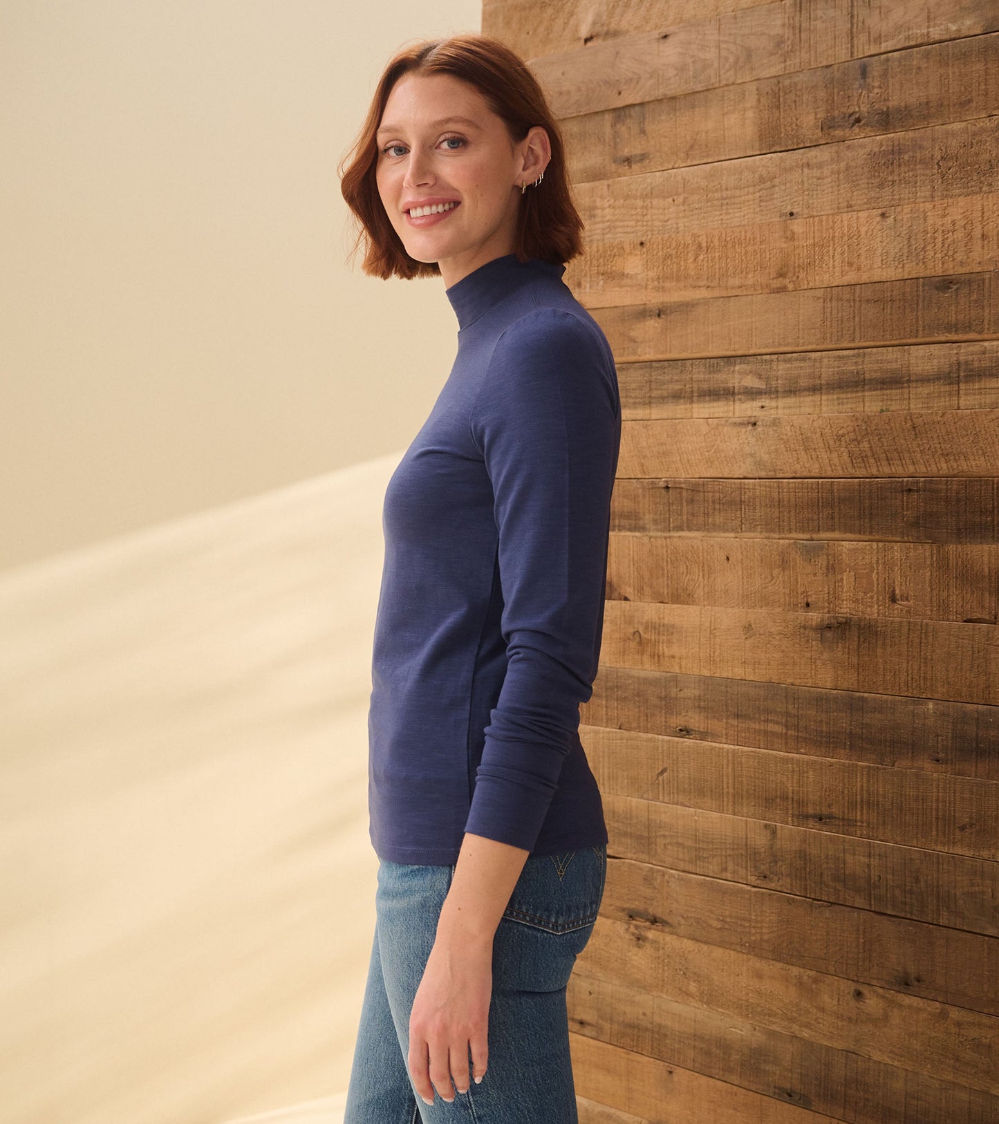 Mock neck top in patriot blue, long sleeves, fitted style, worn with jeans, displayed against a wooden backdrop.