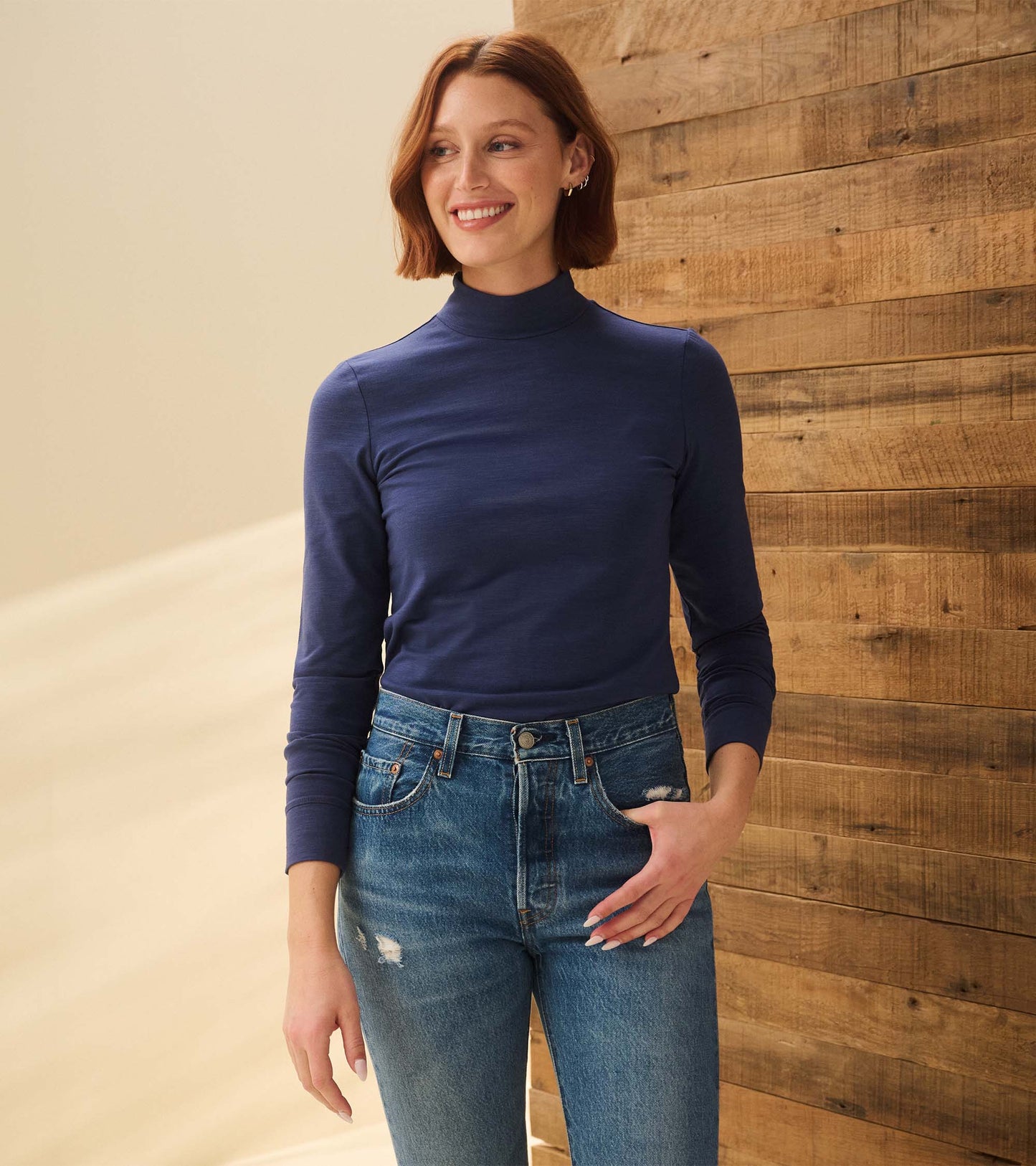 Mock neck top in patriot blue, long sleeves, fitted style, paired with high-waisted distressed jeans.