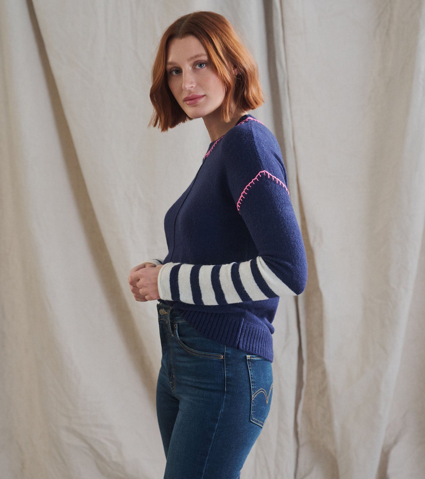 Navy sweater with pink stitching and white striped sleeves, styled with fitted jeans.