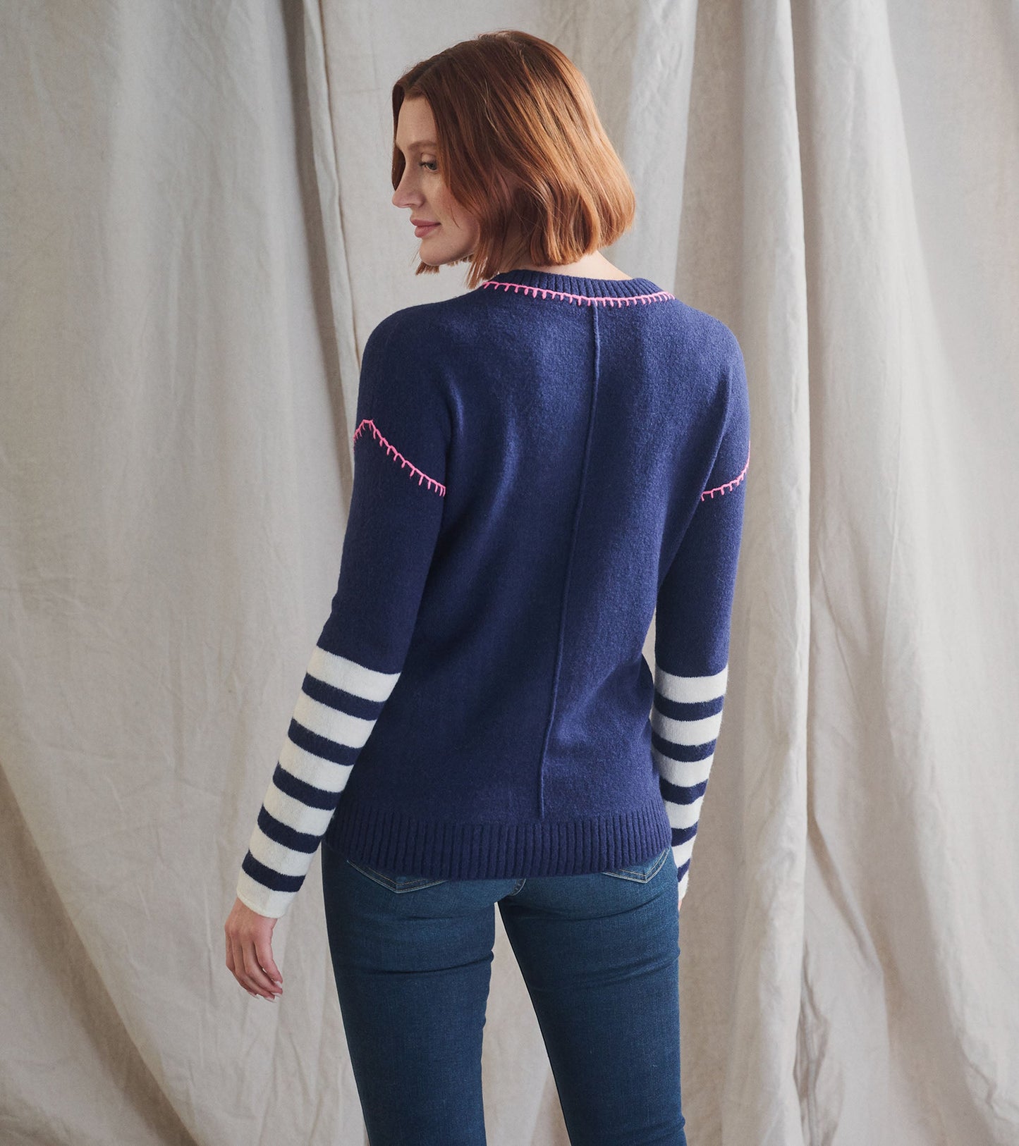 Navy sweater with pink stitching and striped white sleeves, shown from the back.