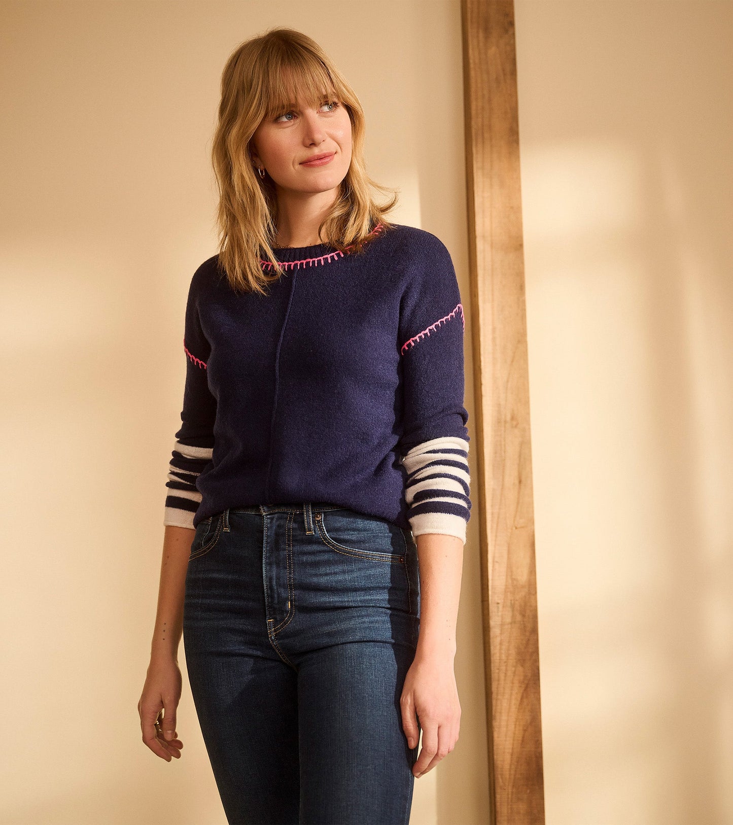 Navy sweater with pink stitching and striped sleeves, styled with dark jeans.