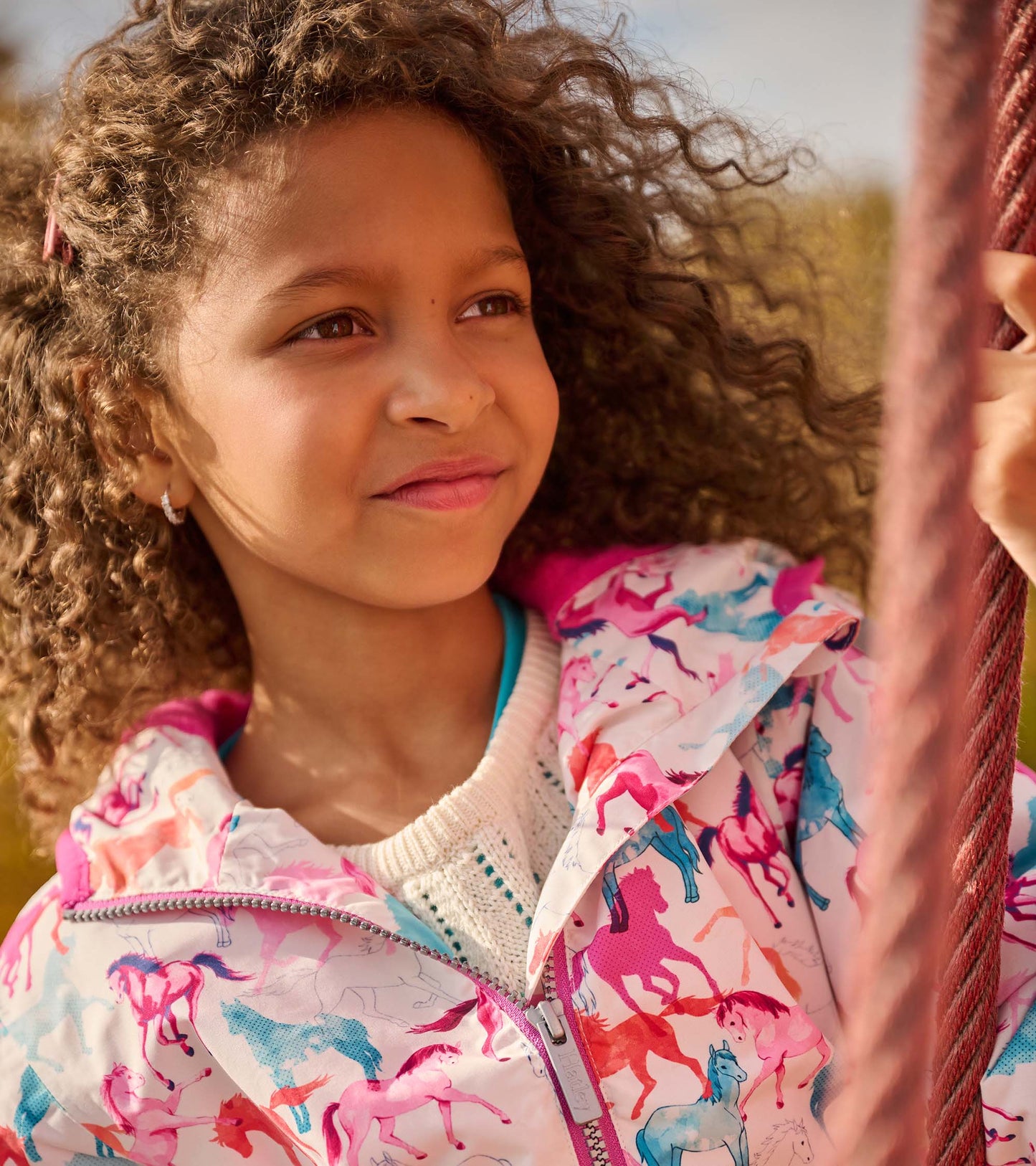 Lightweight zip-up rain jacket featuring a colorful horse print on a white background, perfect for girls.