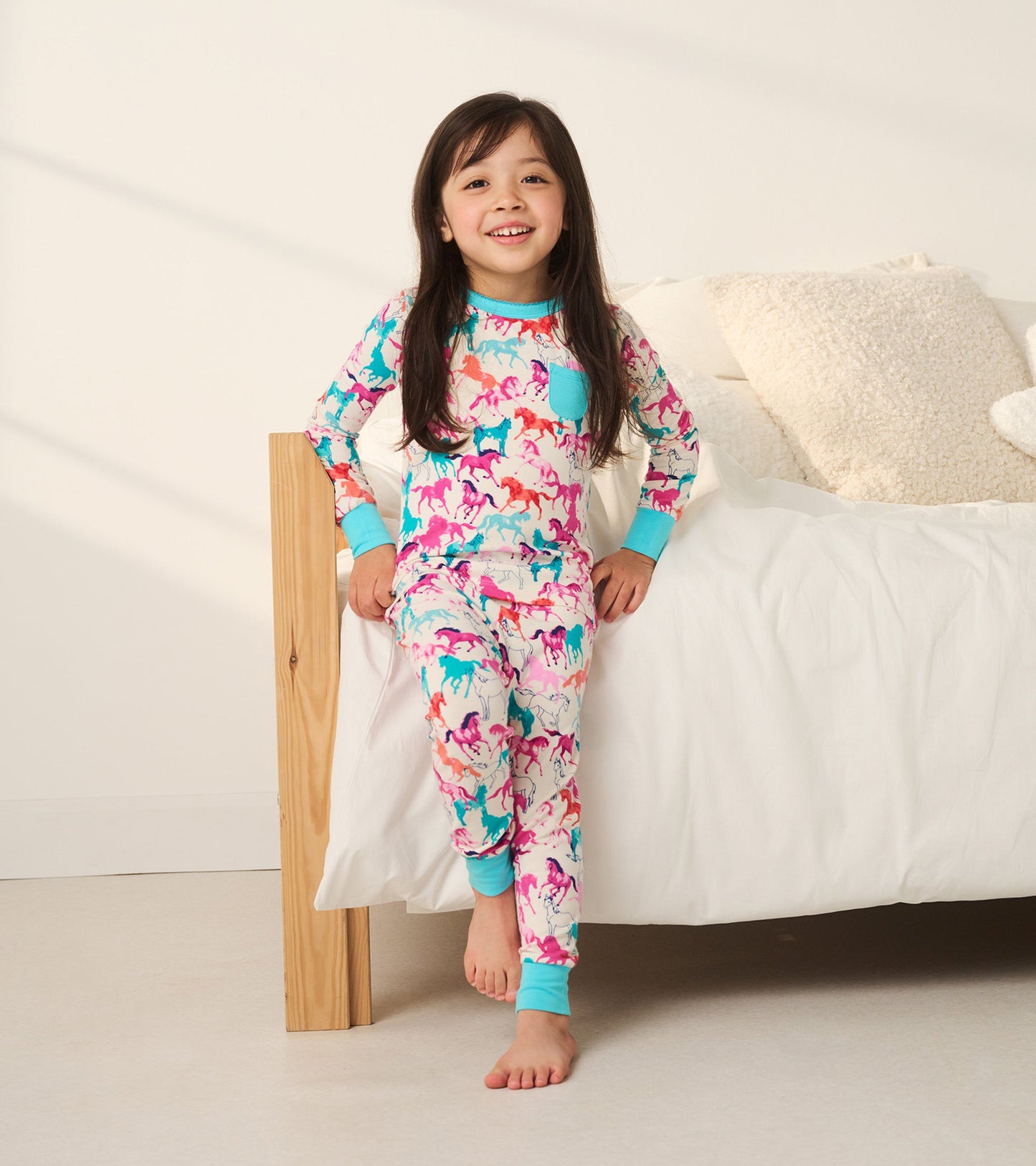 Colorful bamboo pajama set featuring playful horse patterns, with a turquoise trim and a pocket, worn by a smiling girl.