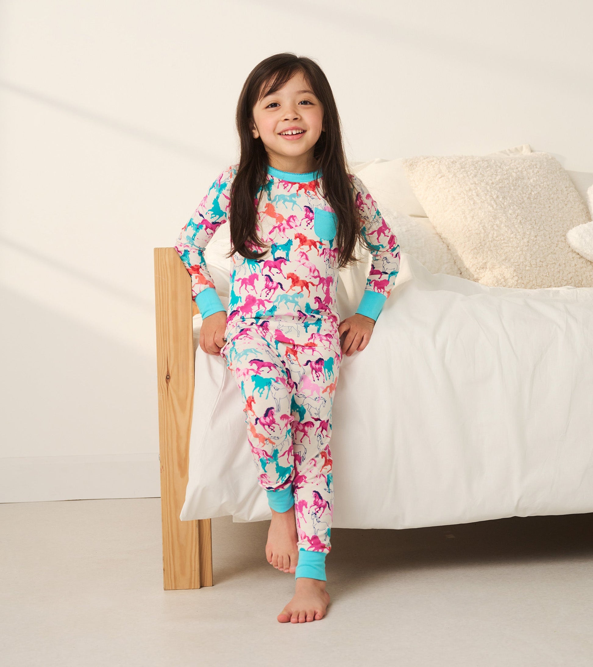 Colorful bamboo pajama set featuring playful horse patterns, with a turquoise trim and a pocket, worn by a smiling girl.
