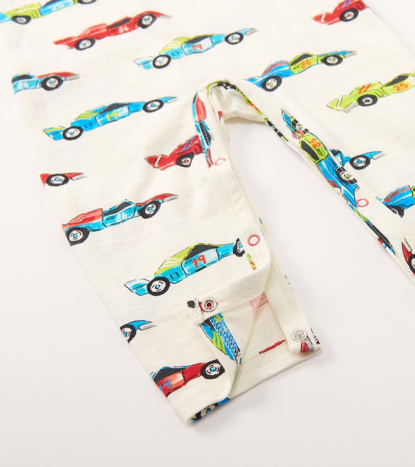 Long sleeve romper featuring a playful watercolor racecar print on a cream background, with snap closures at the bottom.