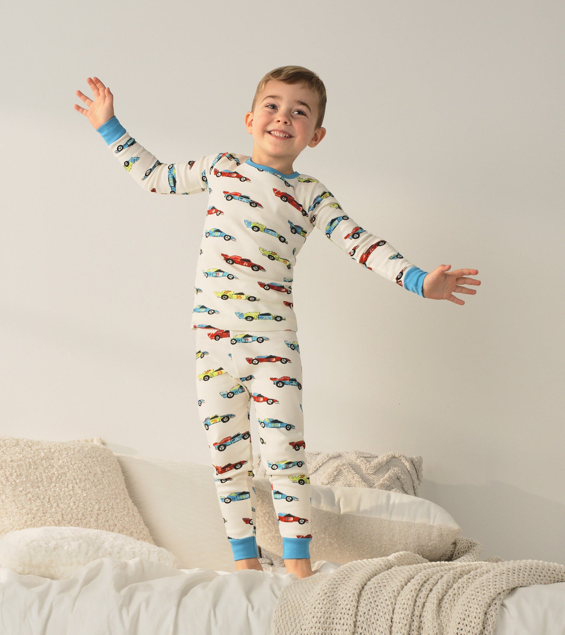 Organic cotton pajama set featuring colorful racecars on a cream background, with blue cuffs and a playful fit.