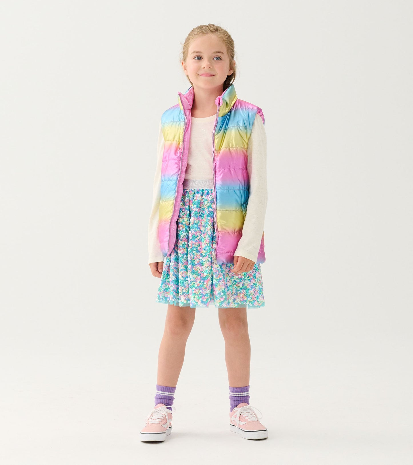 Reversible quilted vest in rainbow colors, worn over a floral skirt, featuring a high collar and zip closure.
