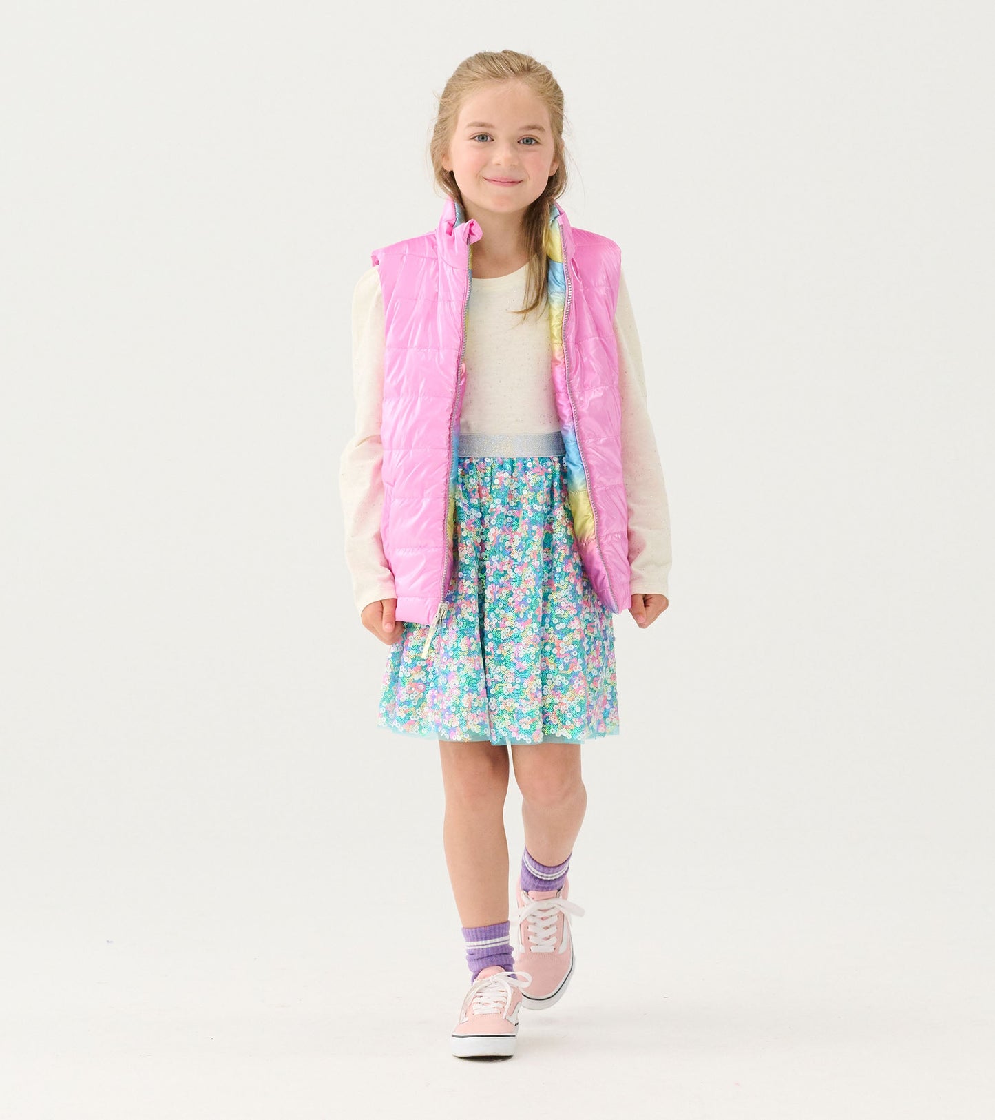 Reversible quilted vest in shiny pink, worn over a floral skirt, perfect for layering in cool weather.