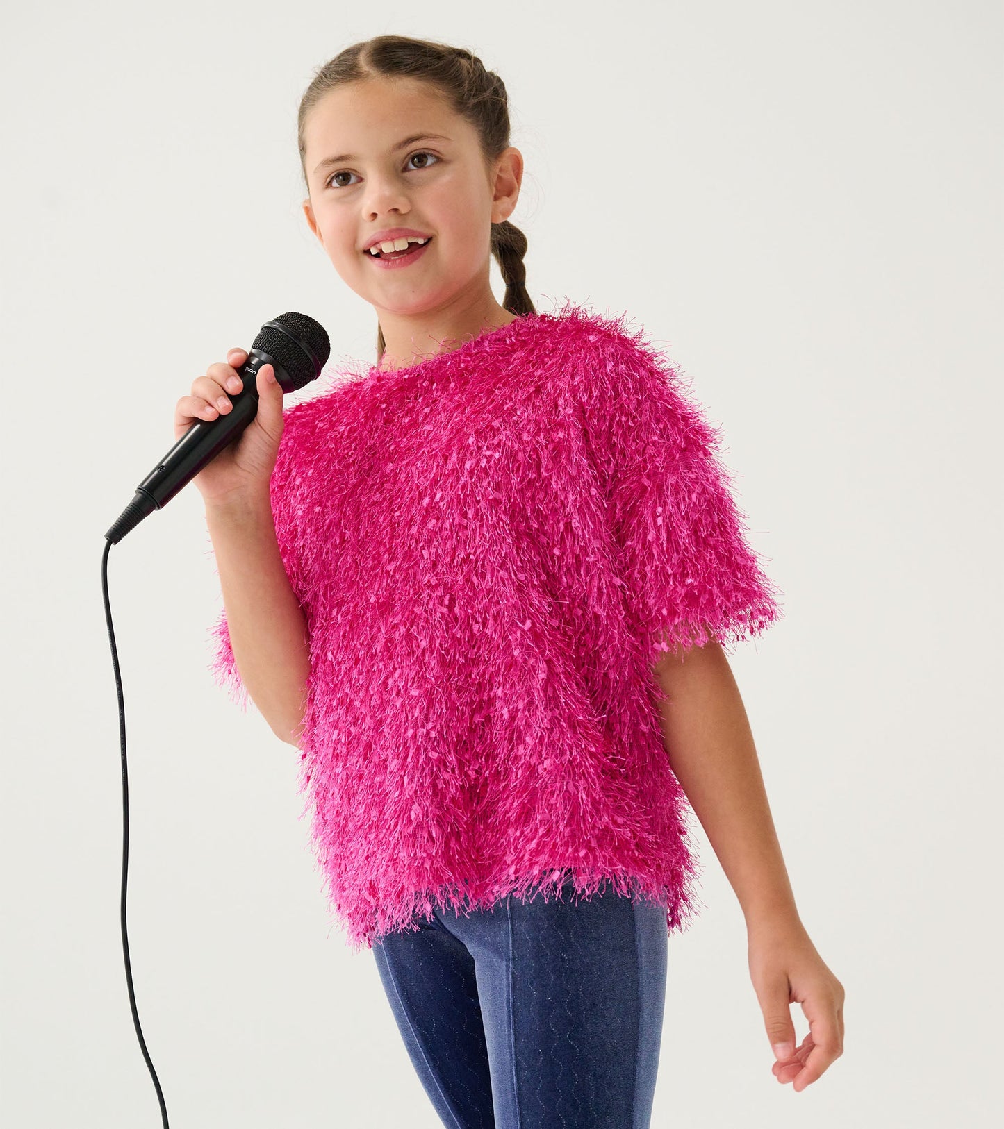 Fluffy pink knit sweater with short sleeves, worn by a girl holding a microphone, paired with dark jeans.