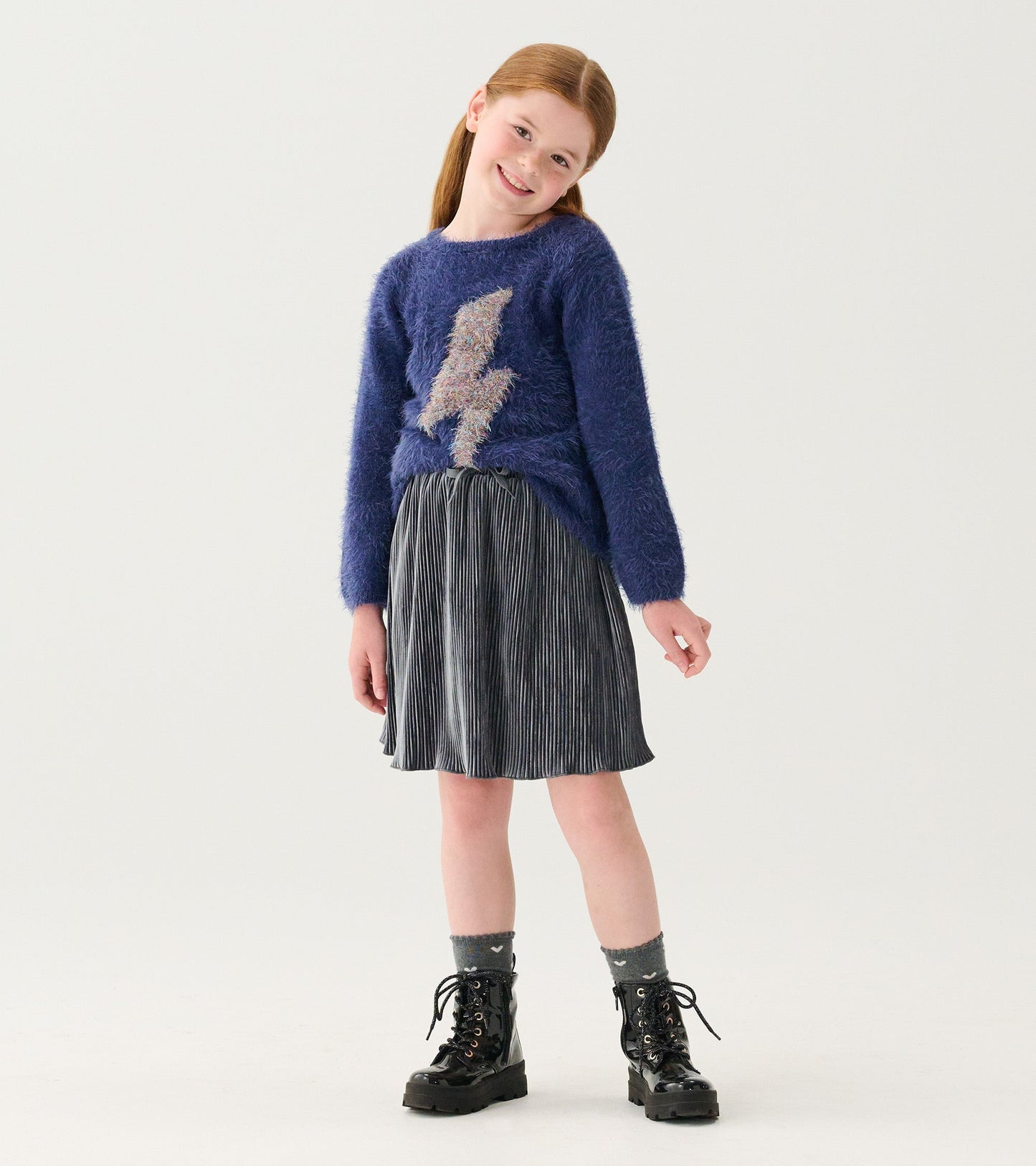 Silver pleated velour skirt with a flared shape, paired with a blue sweater and black boots.