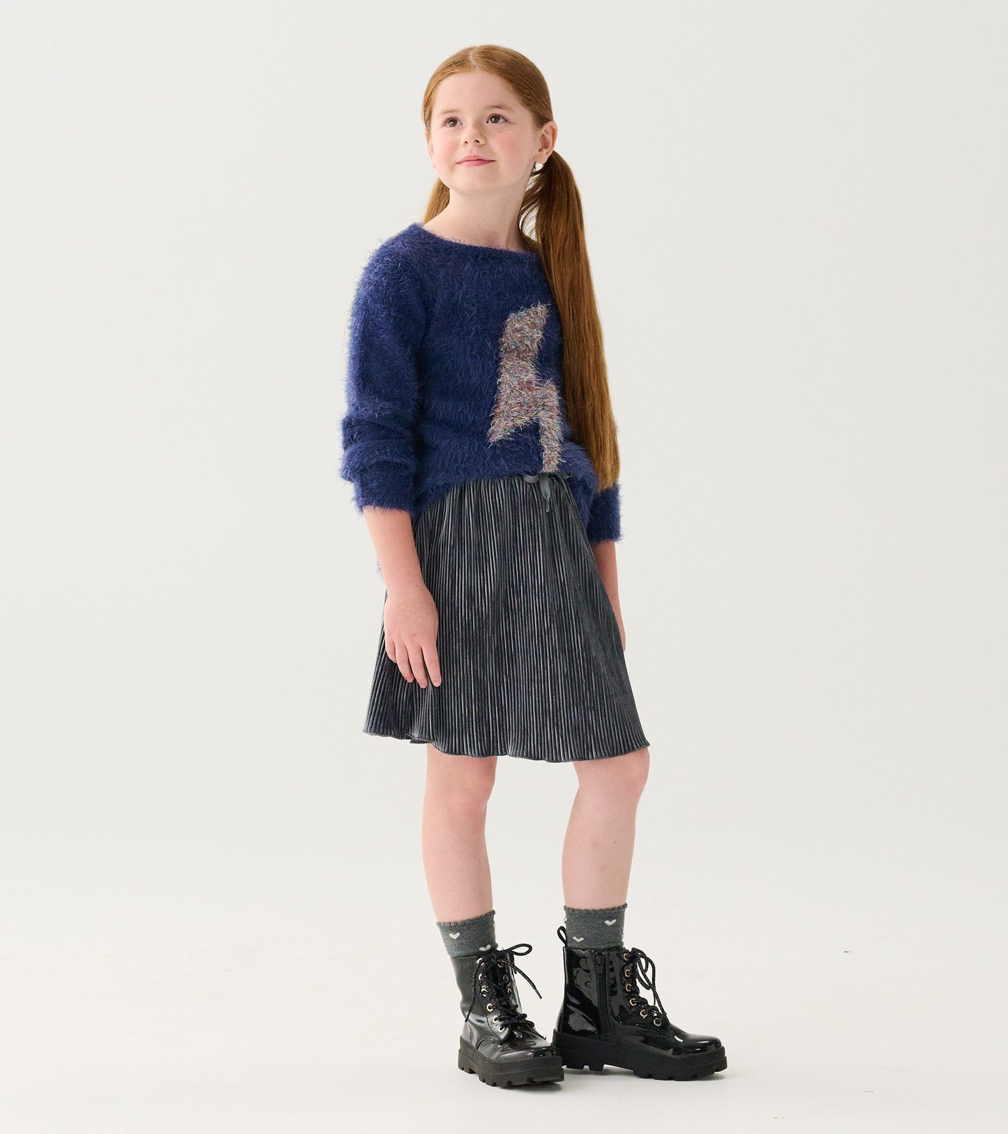 Silver pleated velour skirt with a flared shape, paired with a cozy blue sweater and black lace-up boots.