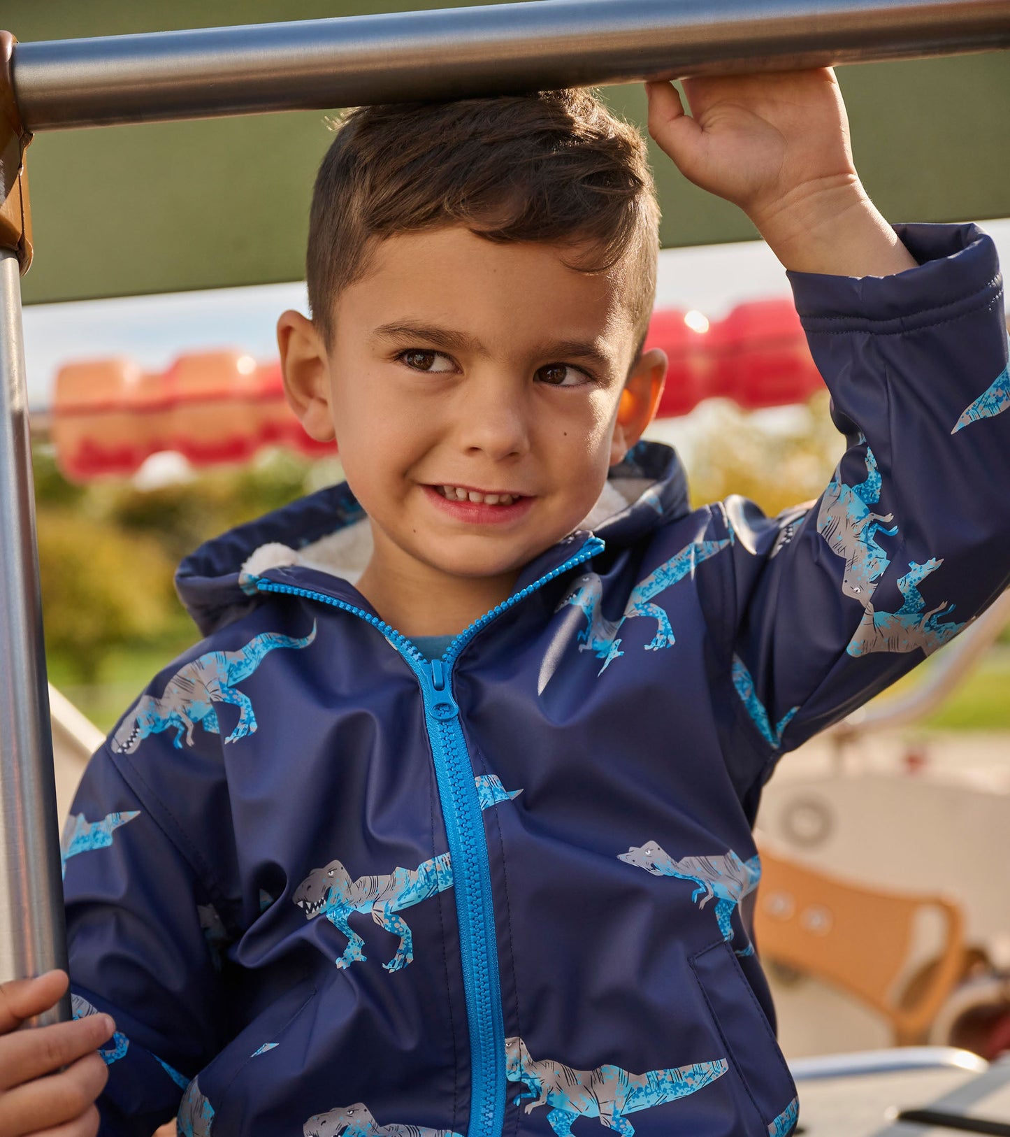 Navy zip-up rain jacket with T-Rex print and sherpa lining, featuring a hood and blue zipper, worn by a smiling boy.