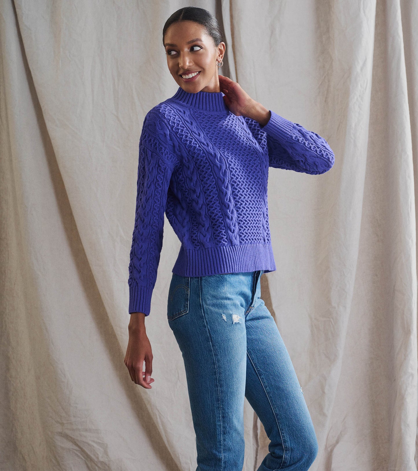 Ultra violet button neck sweater with cable knit pattern, paired with distressed blue jeans, styled casually.