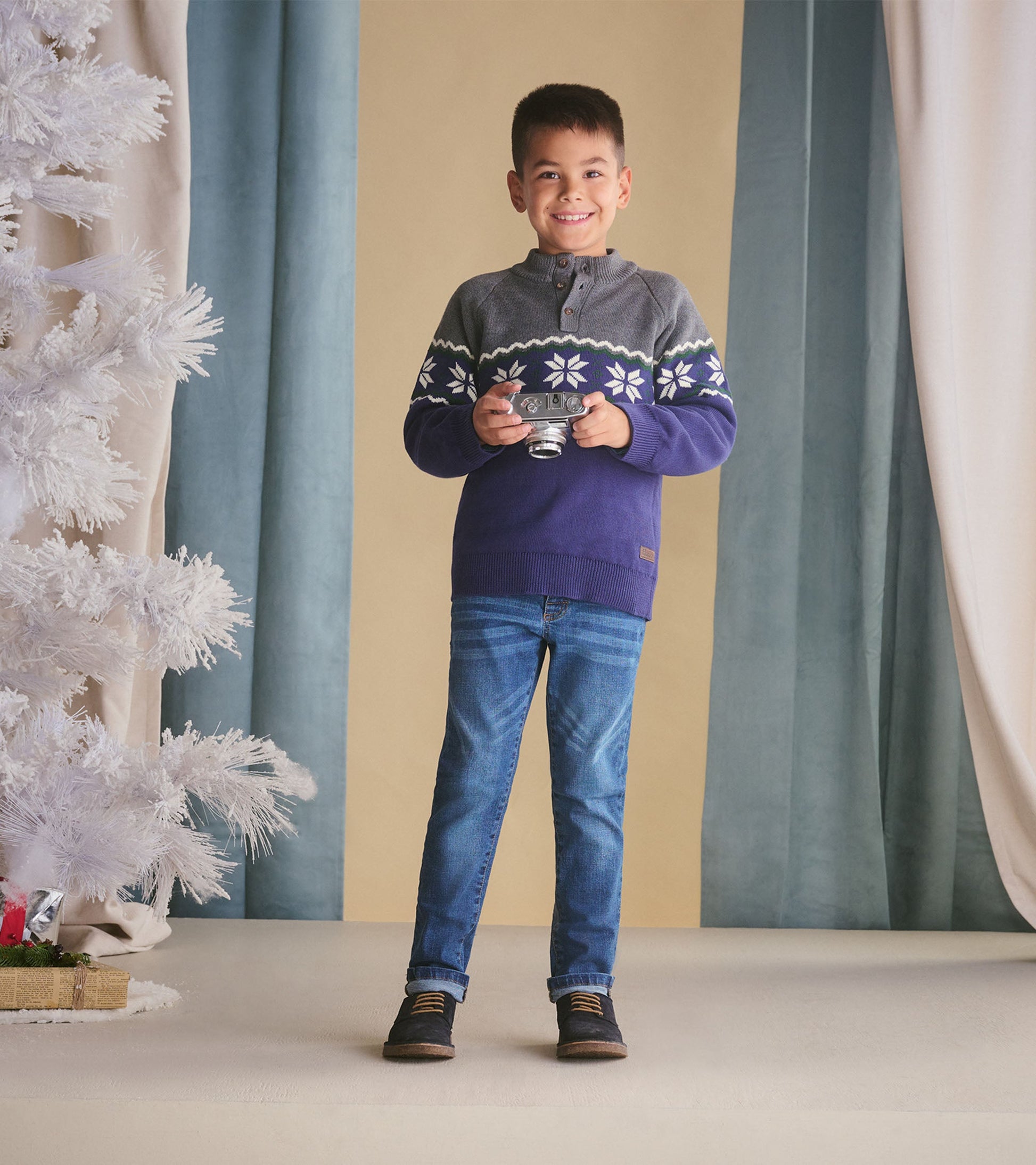 Knit mockneck sweater in gray and navy with snowflake pattern, perfect for winter wear. Styled with jeans and a camera.