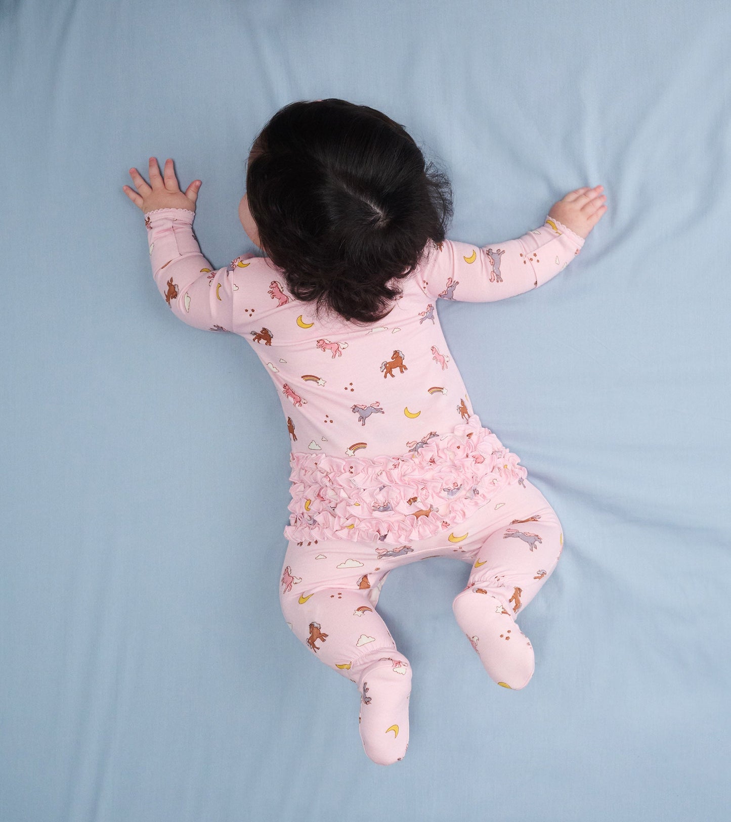 Pink bamboo sleeper with whimsical pony print and ruffle bum, designed for baby girls, shown from above.