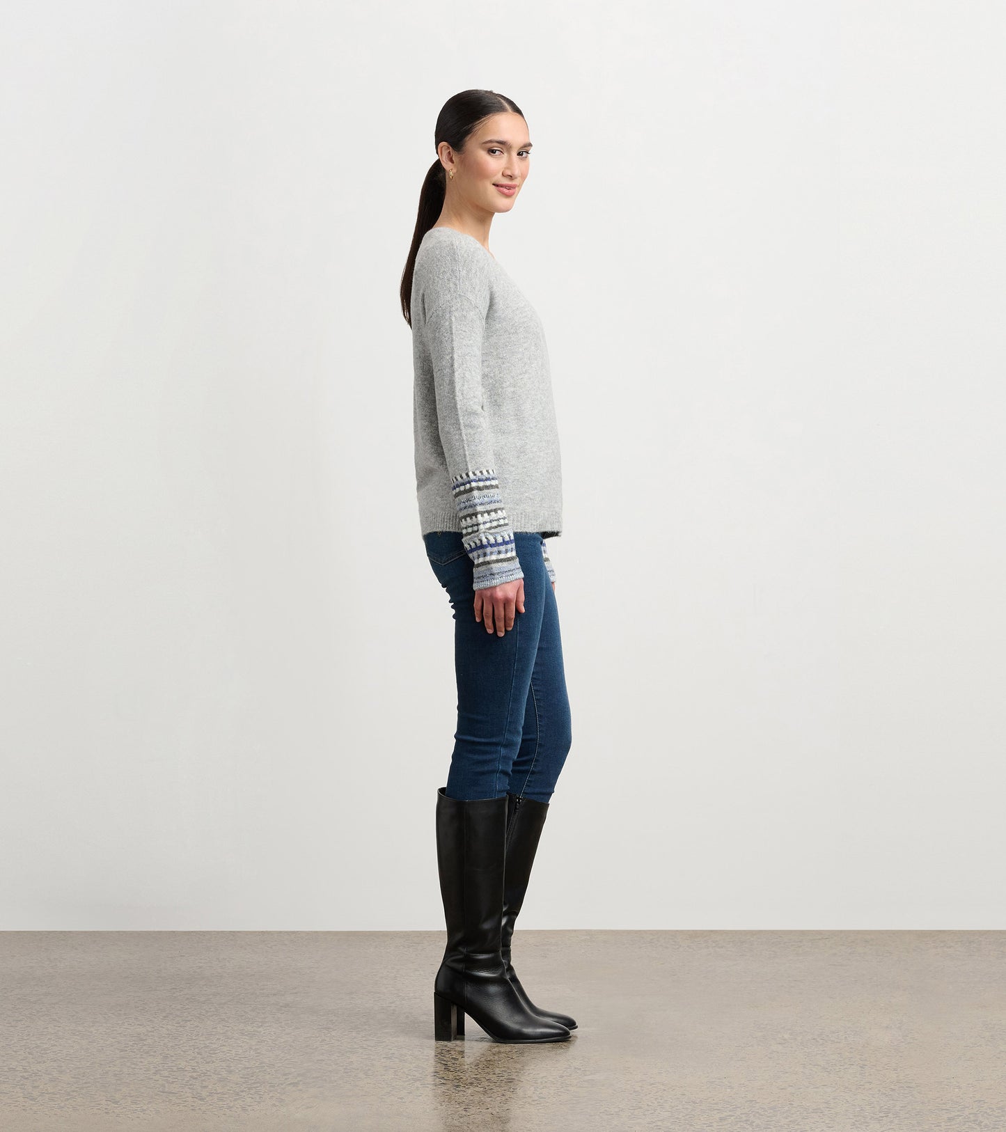 Grey melange sweater with patterned cuffs, featuring a relaxed fit and long sleeves, styled with jeans and knee-high boots.