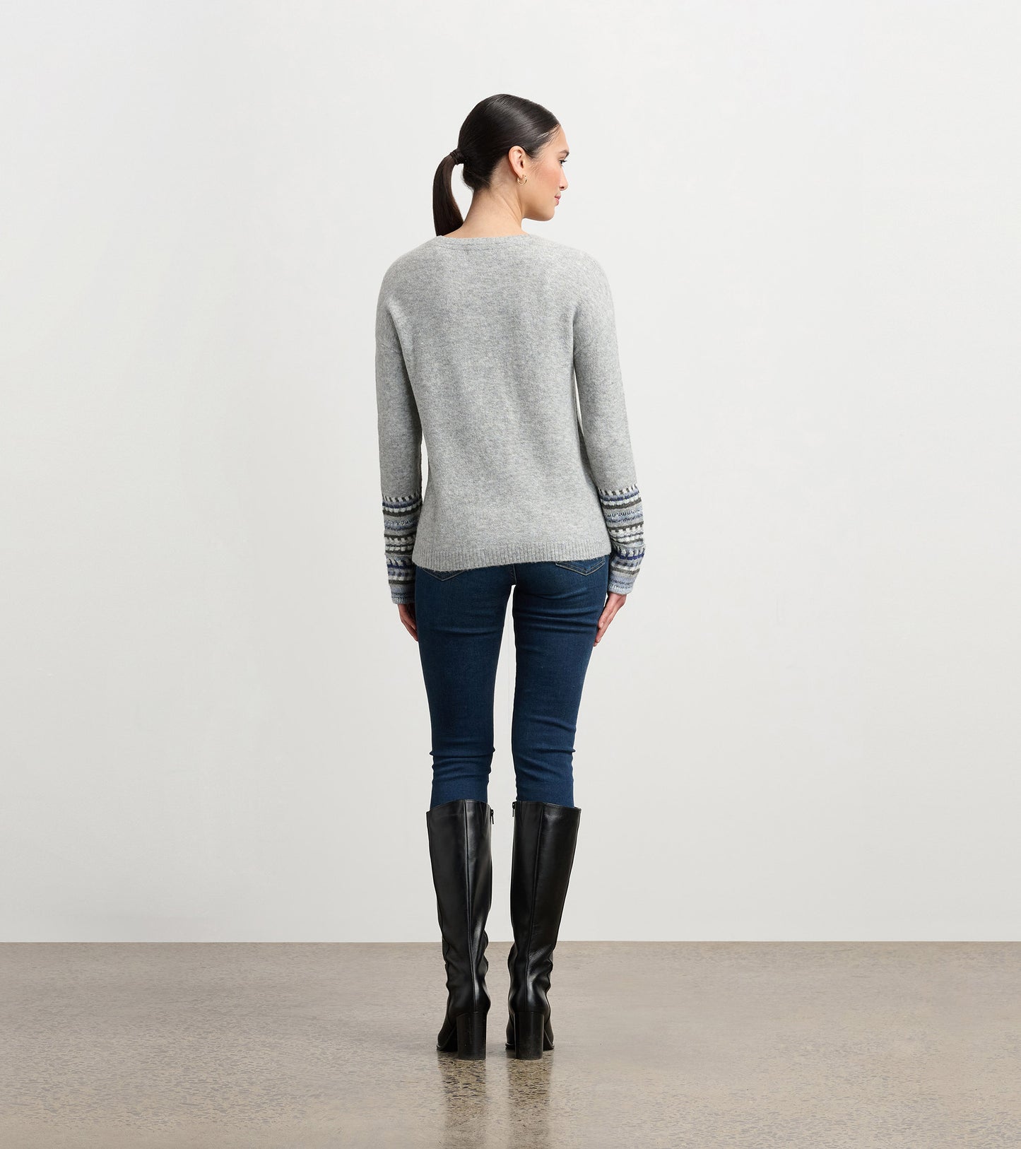 Grey melange sweater with patterned cuffs, fitted shape, and long sleeves, worn with dark jeans and knee-high boots.